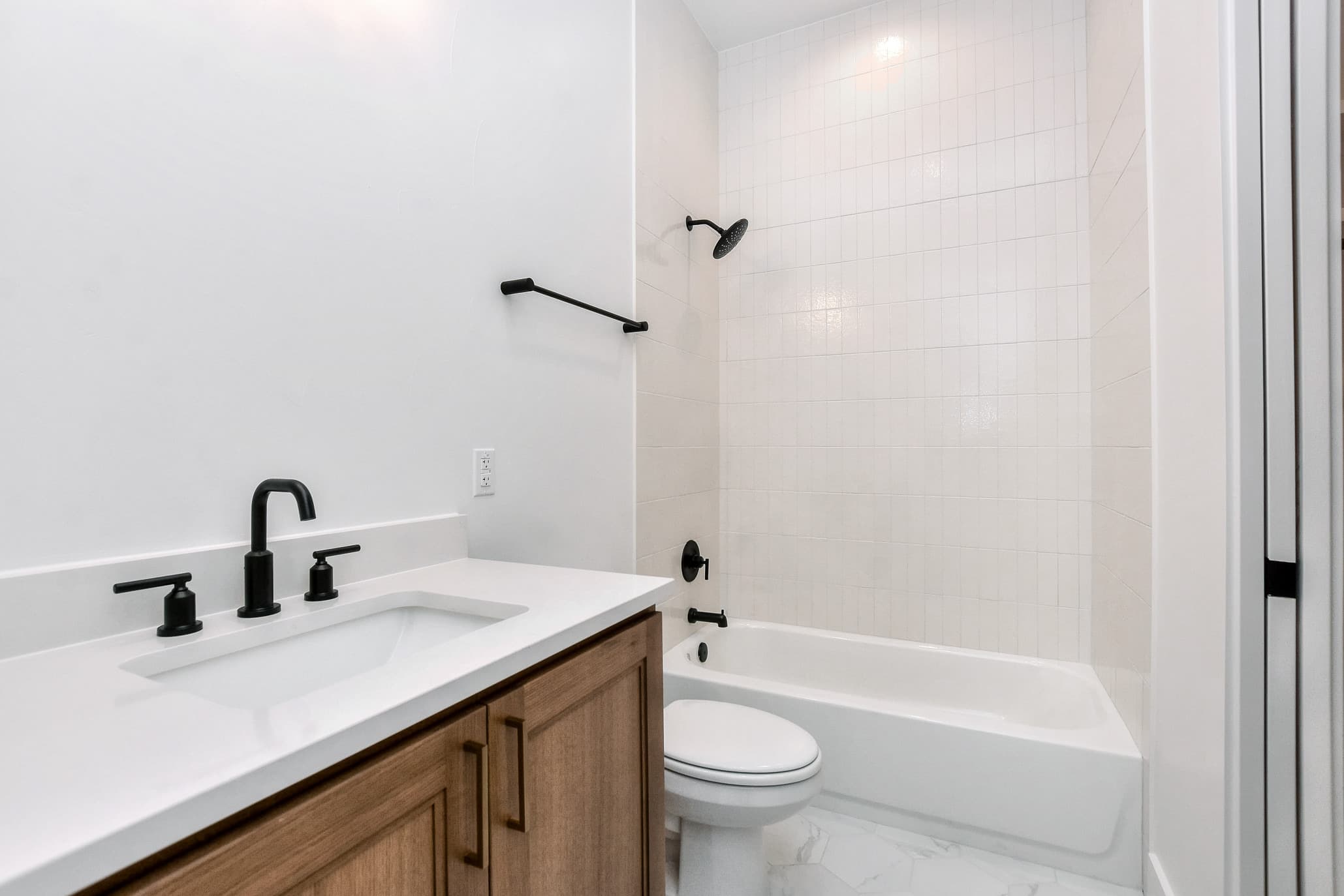 Bathroom with a wood vanity, white quartz counter, black faucet and a tub-shower with white tile