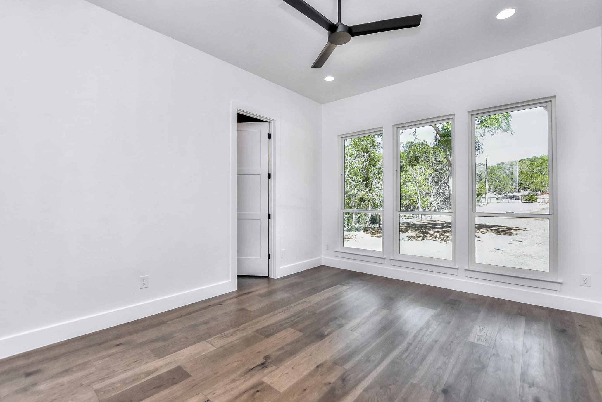 Bedroom with a ceiling fan, white walls and three windows onto wooded views