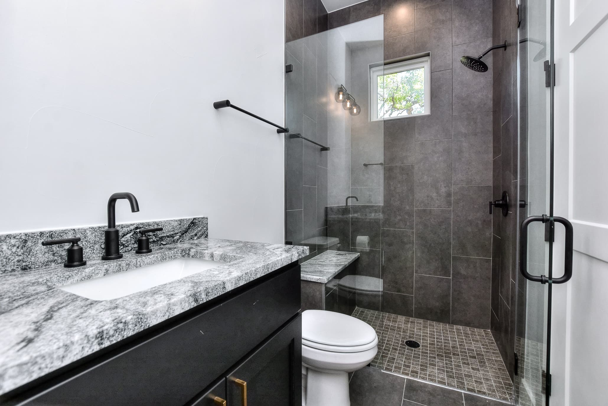 Bathroom with a granite-top vanity, black fixtures and a glass-enclosed tile shower