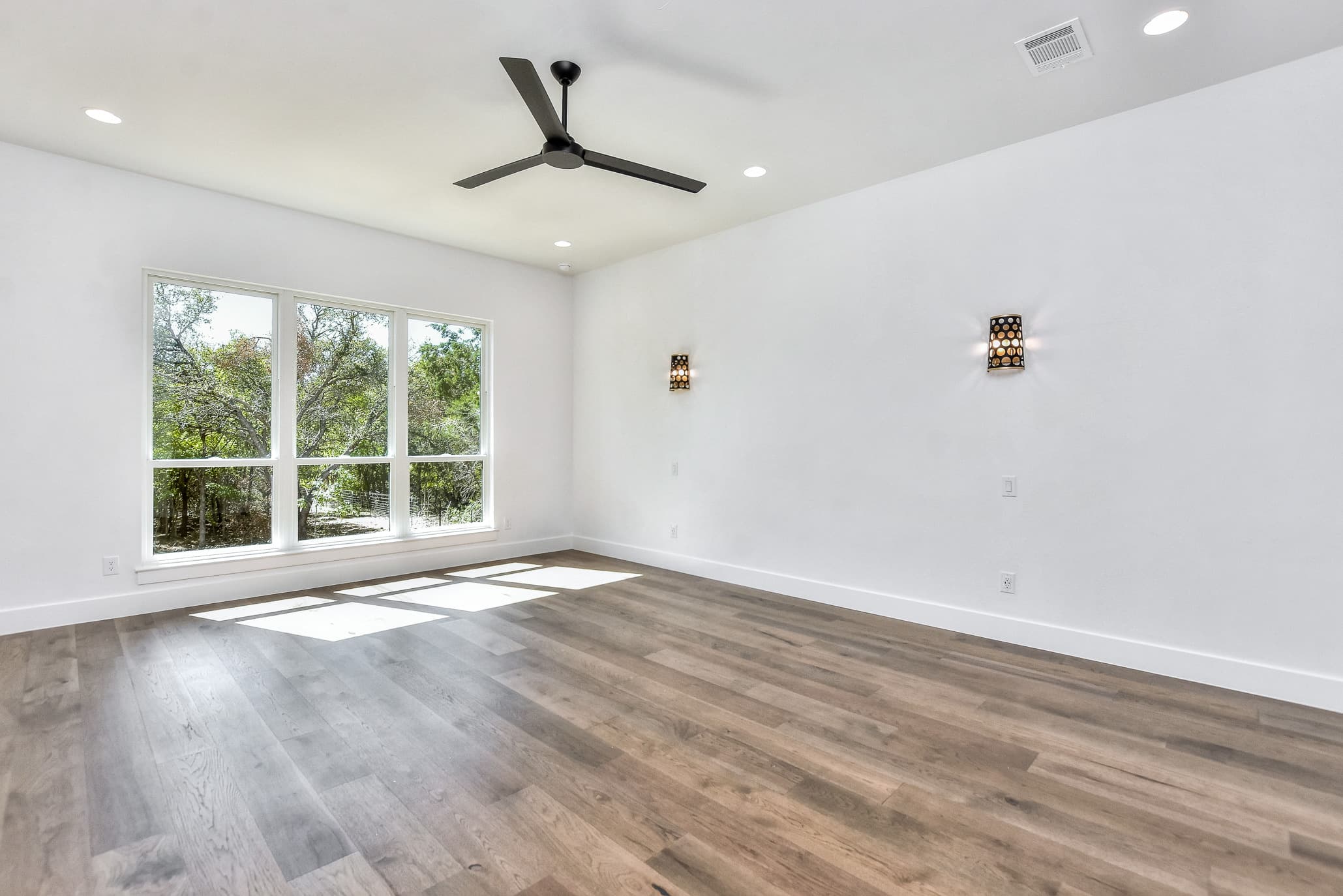 Bedroom with a ceiling fan, wall sconces and large windows to the trees