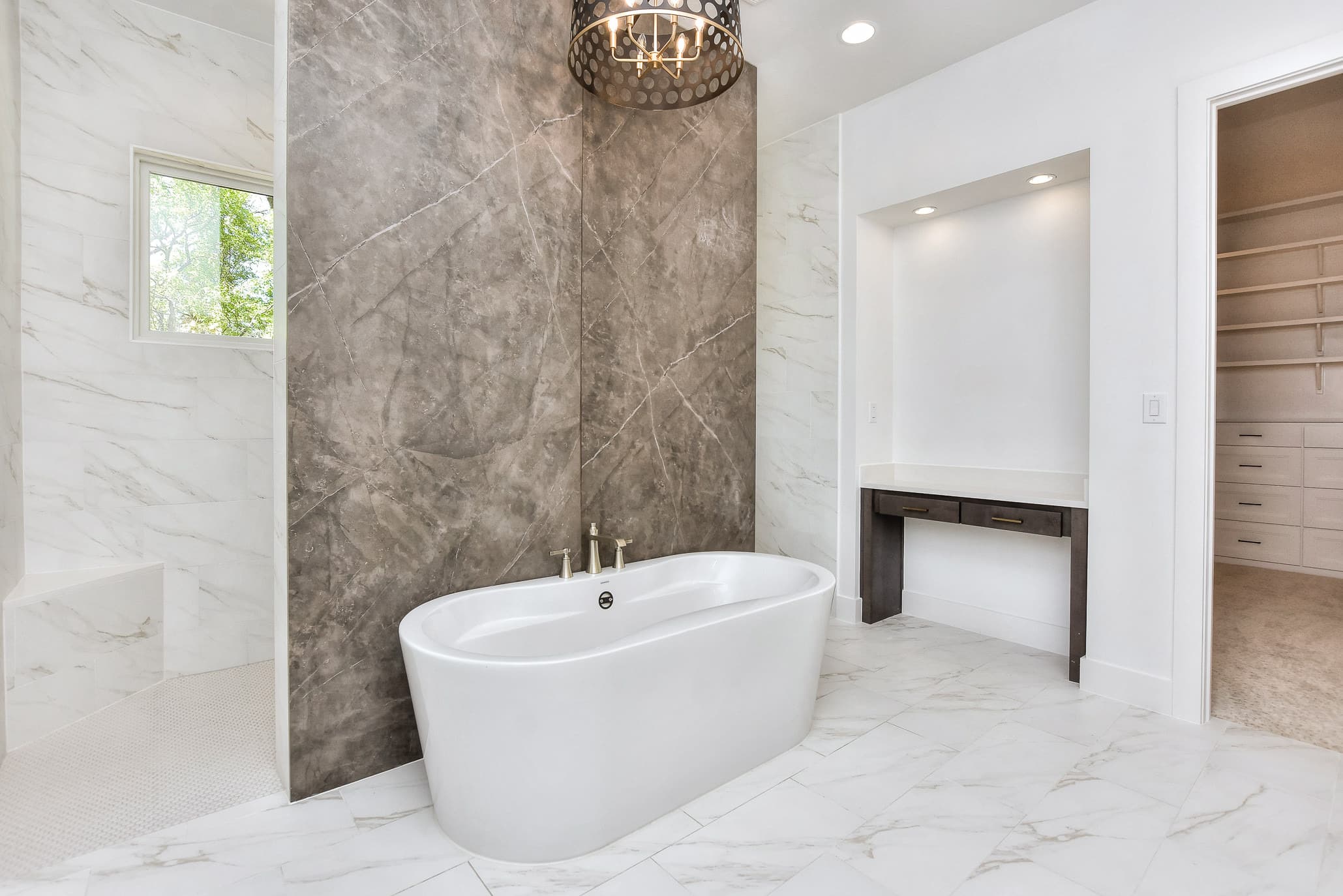 Primary bath with a freestanding tub in front of a large stone-look feature wall and a chandelier