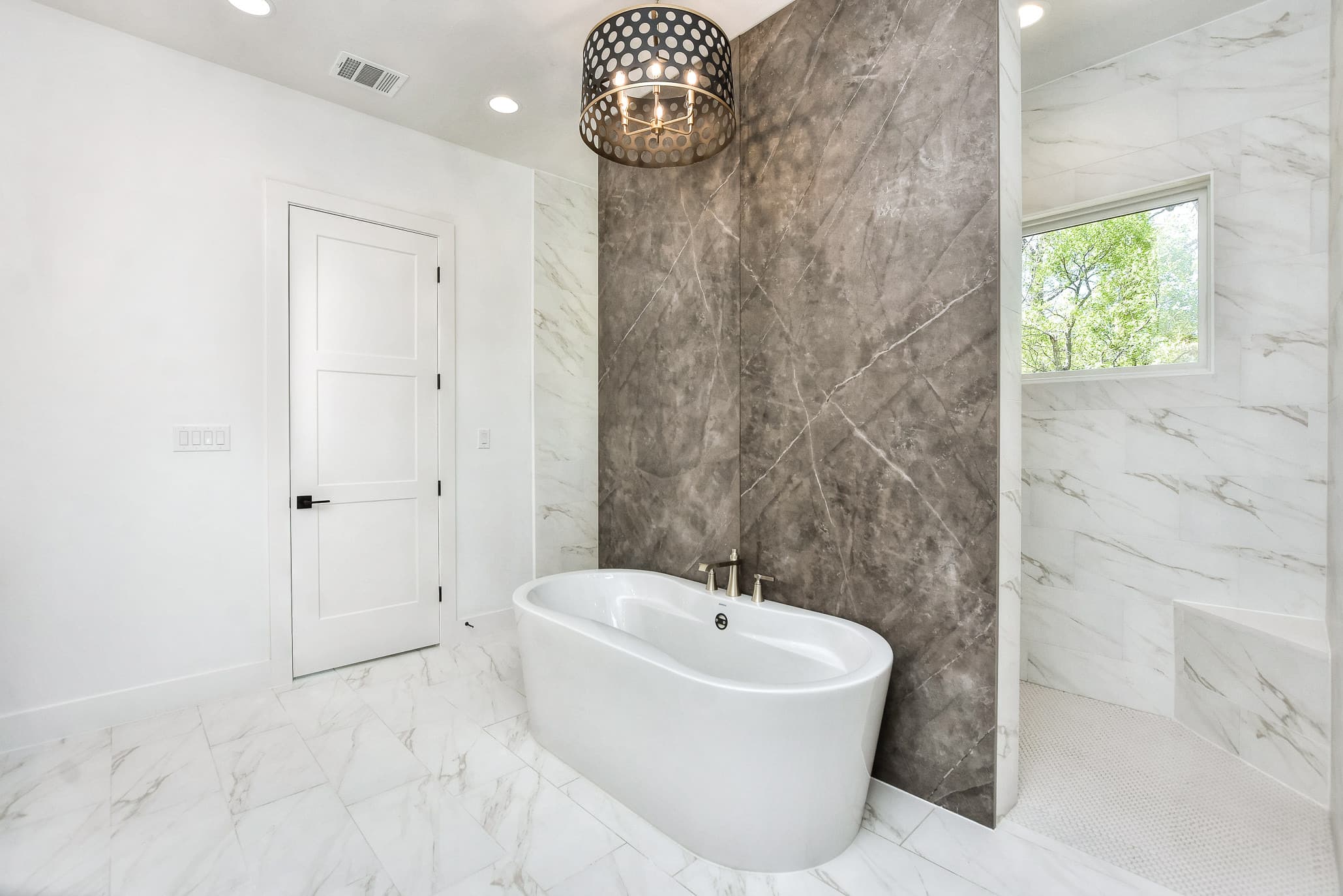 Freestanding tub framed by marble-look walls with a pendant light, and a glass-paned door
