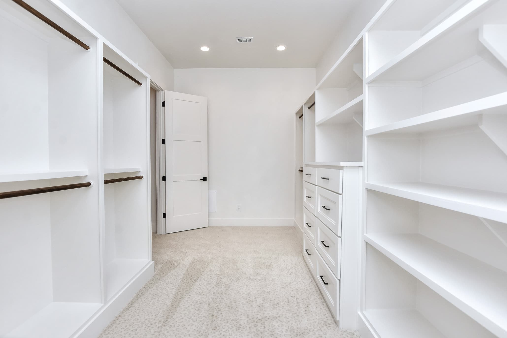 Walk-in closet with built-in drawers and white shelving leading to a door