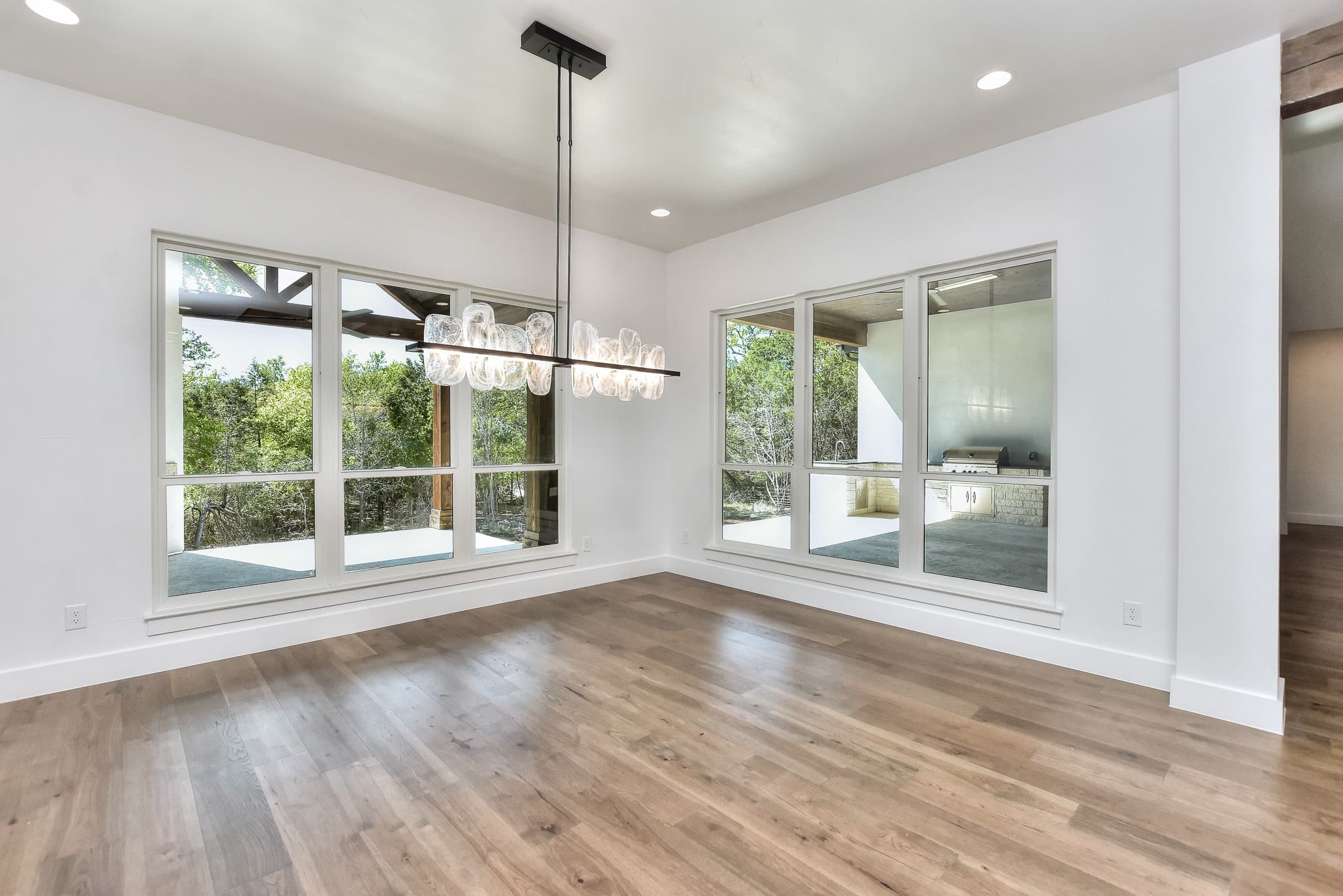 Dining room with a long modern chandelier and windows onto the covered patio and trees