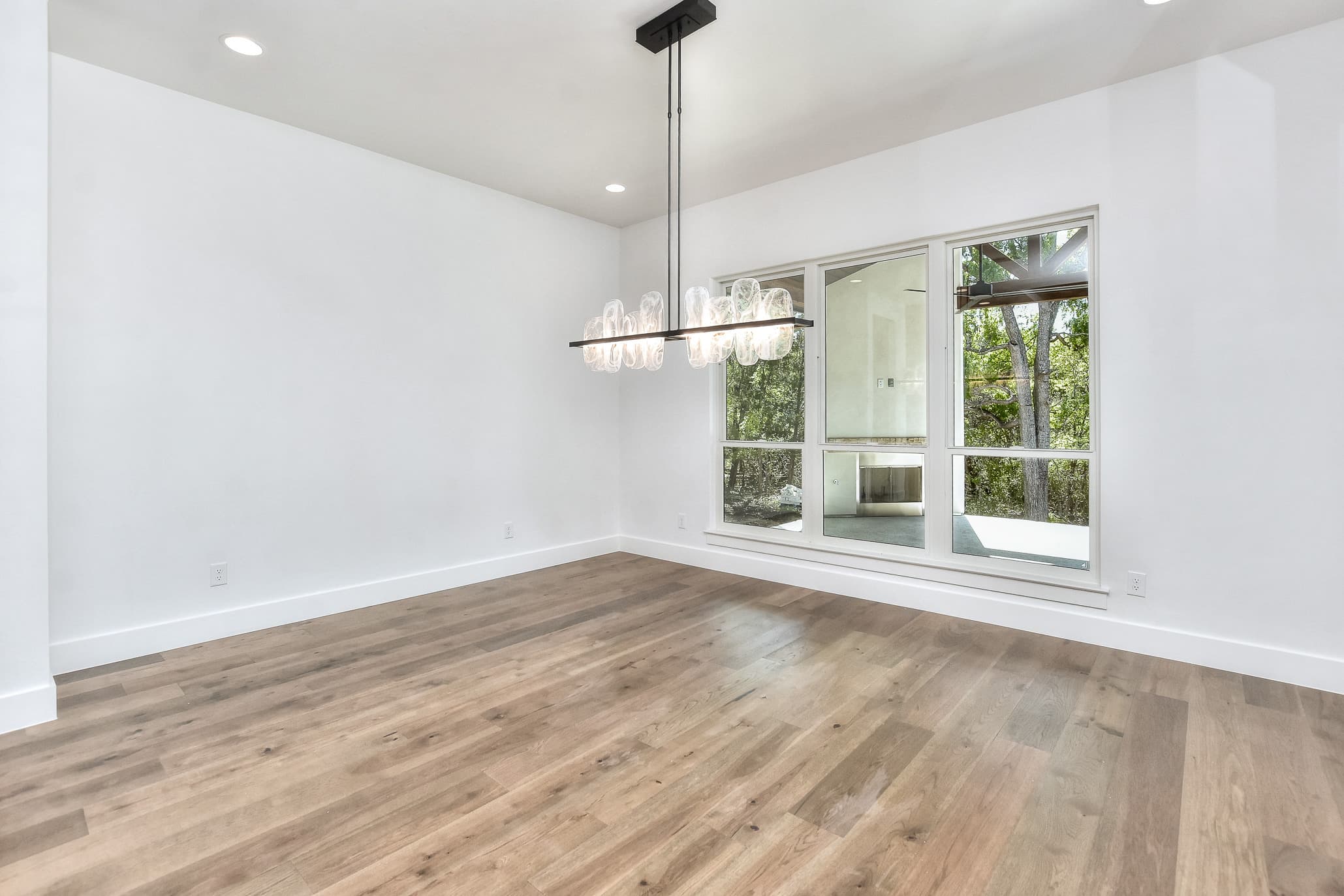 Dining room with a linear glass chandelier, hardwood floors and large windows