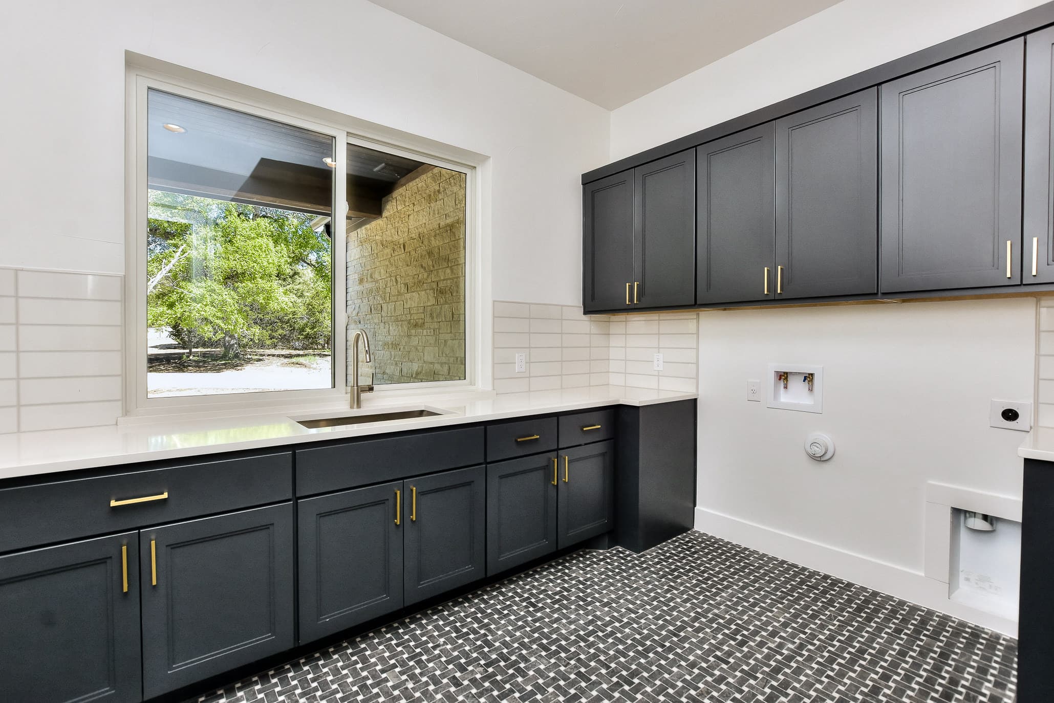 Laundry room with navy cabinetry, brass pulls, white counters and patterned black-and-white tile floor