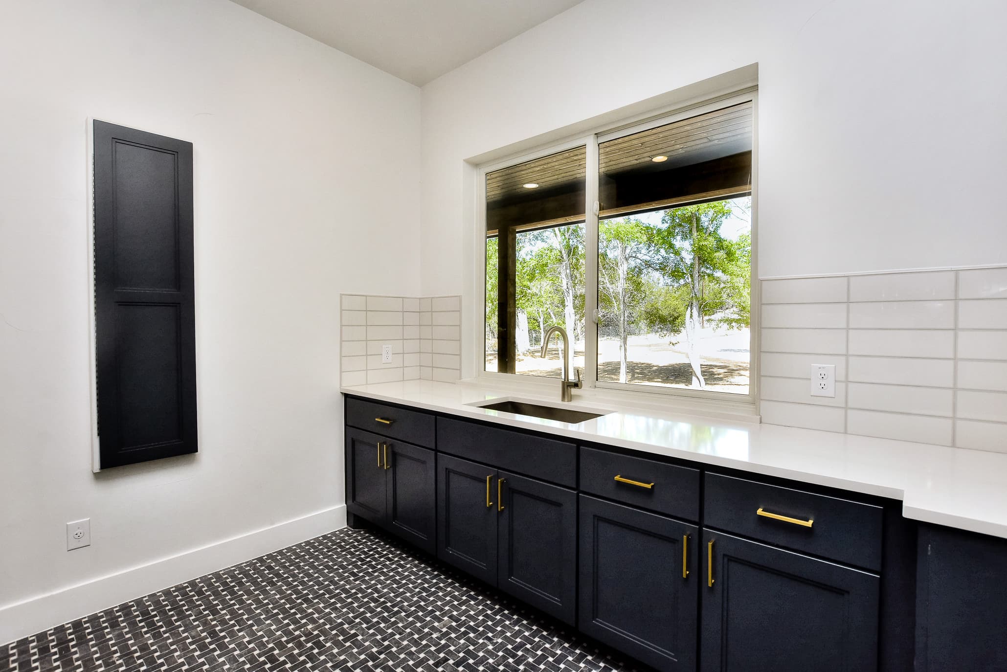 Laundry room with a sink under a window, dark cabinets and a drying cabinet door