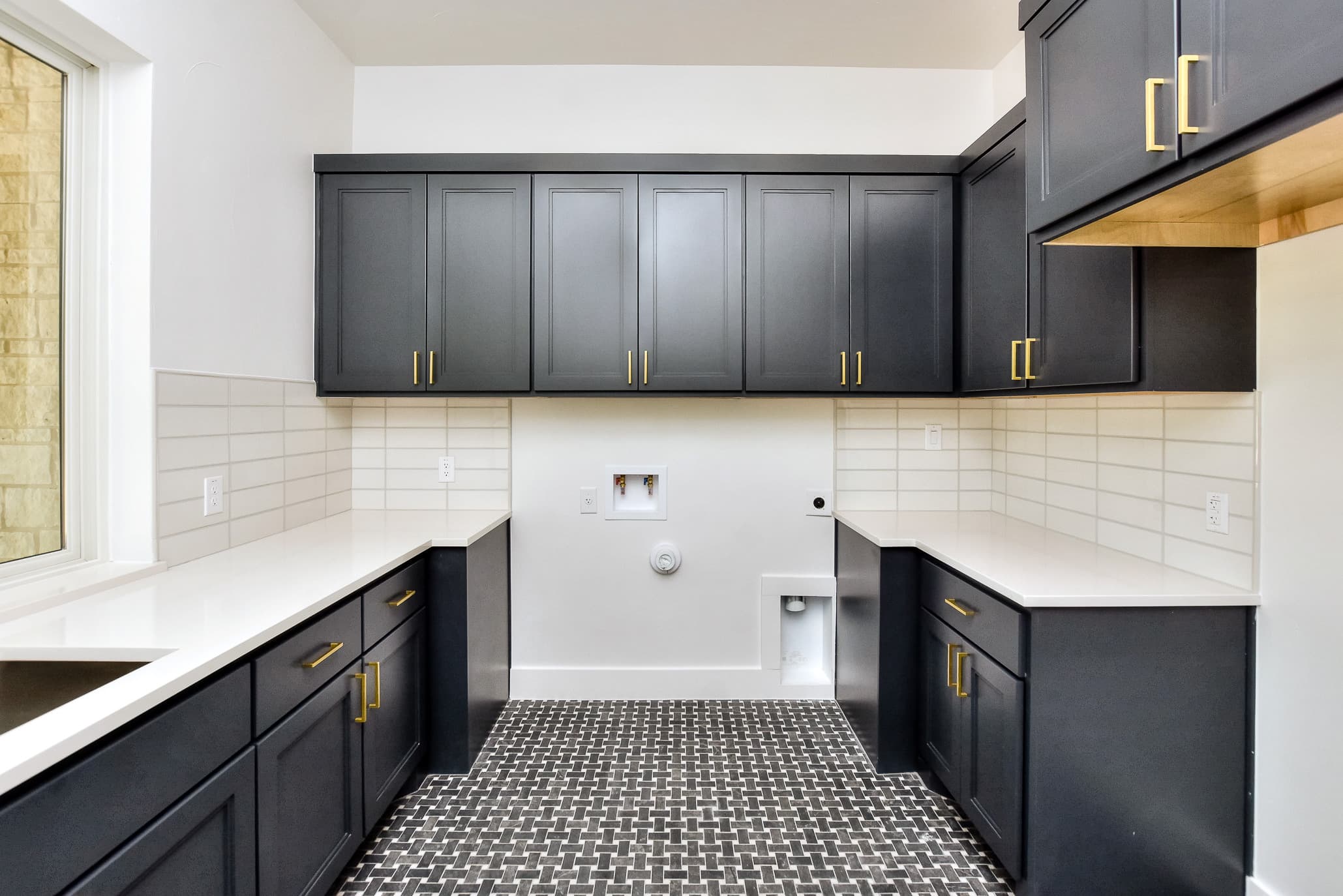 Laundry room cabinets in navy with brass pulls, subway tile backsplash and patterned tile floor