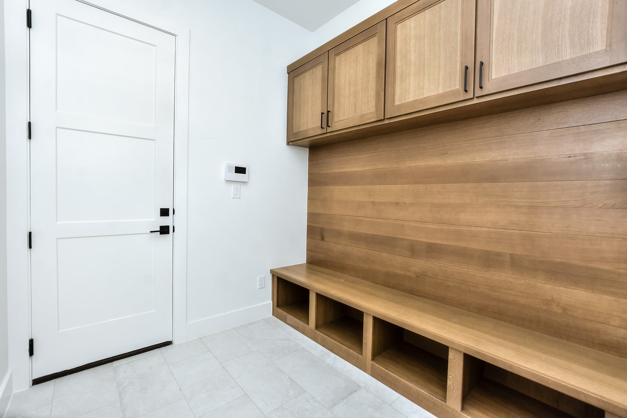Mudroom with a wood-paneled bench, cubbies and upper cabinets beside a white exterior door