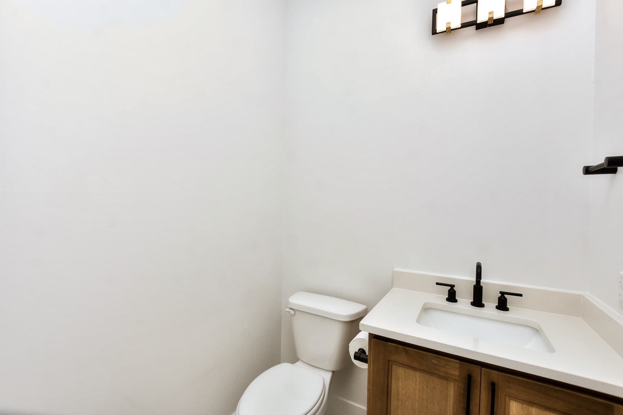 Powder room with a wood vanity, white counter and black faucet