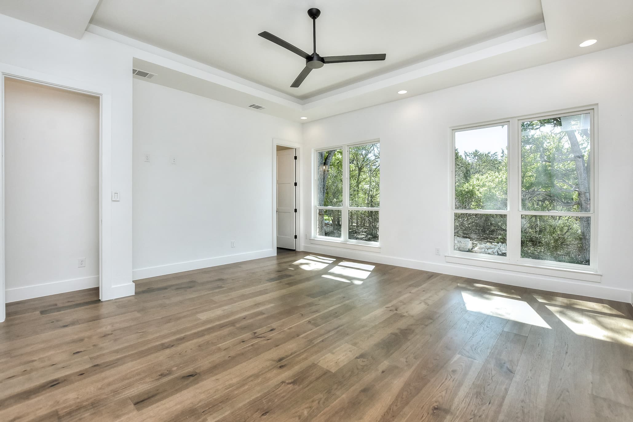 Open living area with a tray ceiling, ceiling fan and windows onto the trees