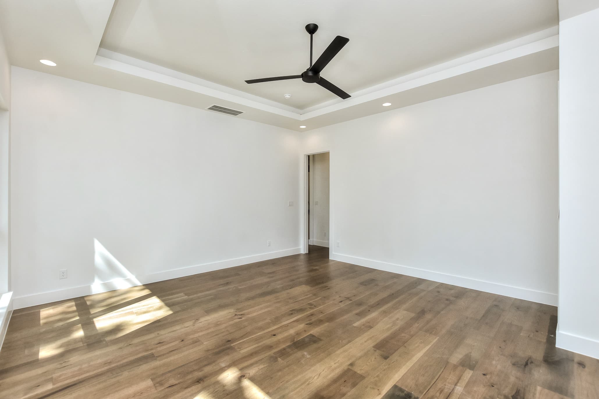Living room with a tray ceiling and black ceiling fan over hardwood floors