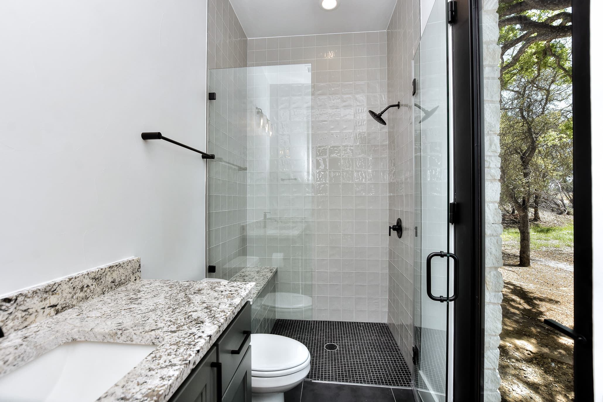 Bathroom with granite vanity top and a glass-enclosed shower with white tile and black fixtures