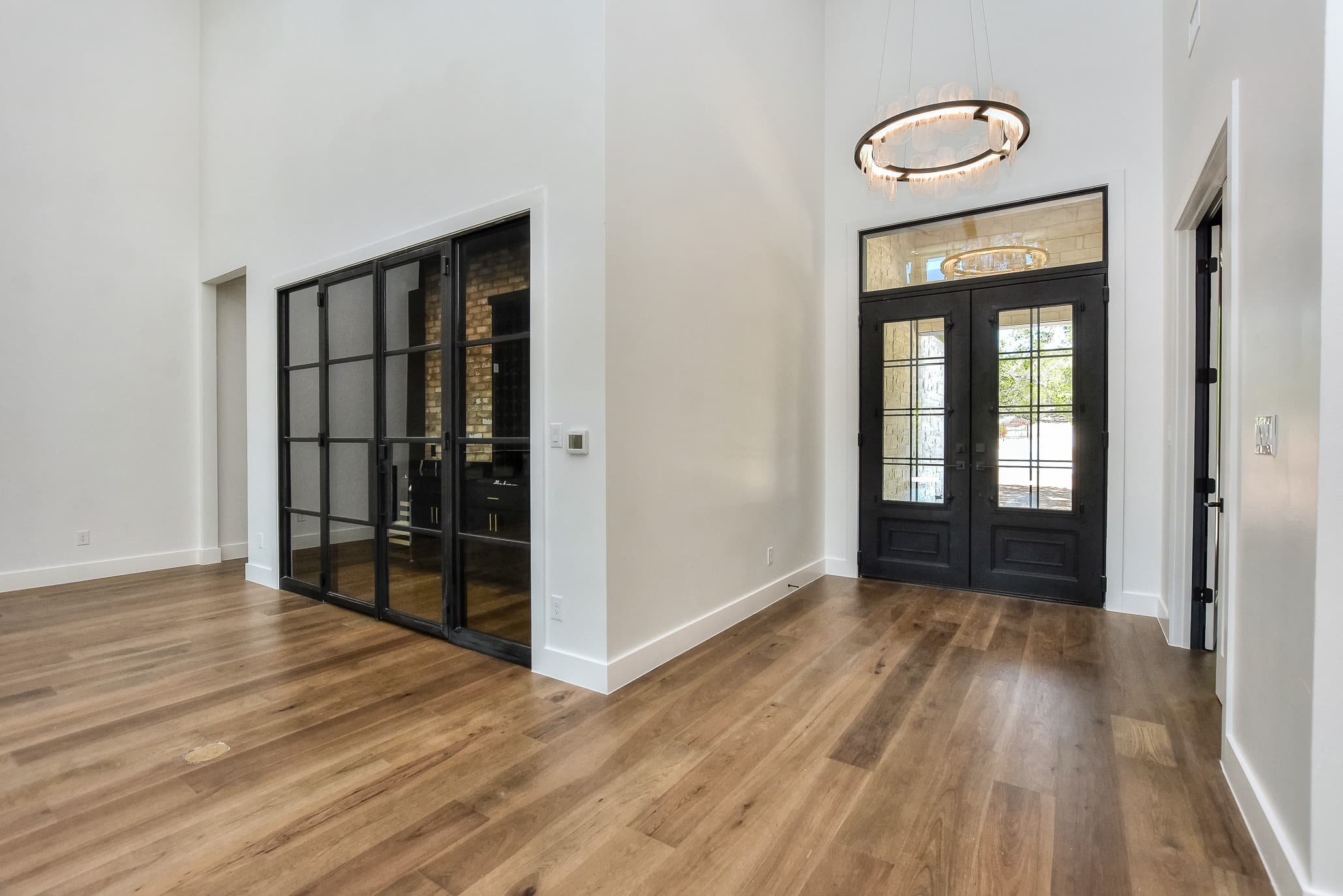 Front entry with black double doors, a ring chandelier and a steel-framed glass wine room