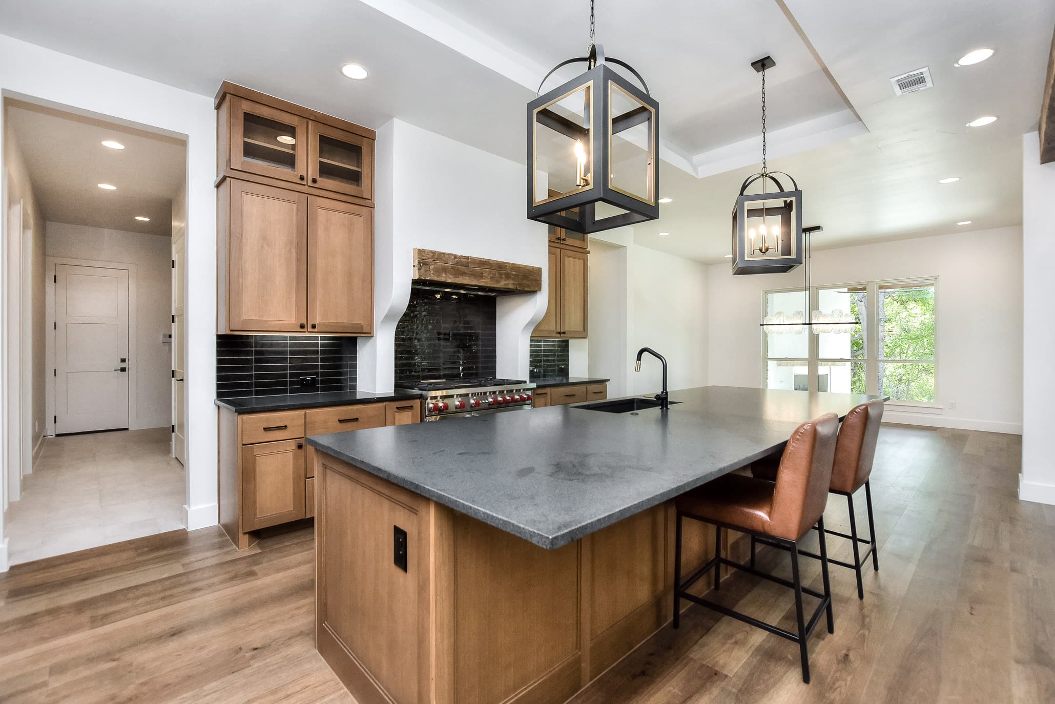 Kitchen with a wood island, leather counter stools, black tile backsplash and lantern pendants