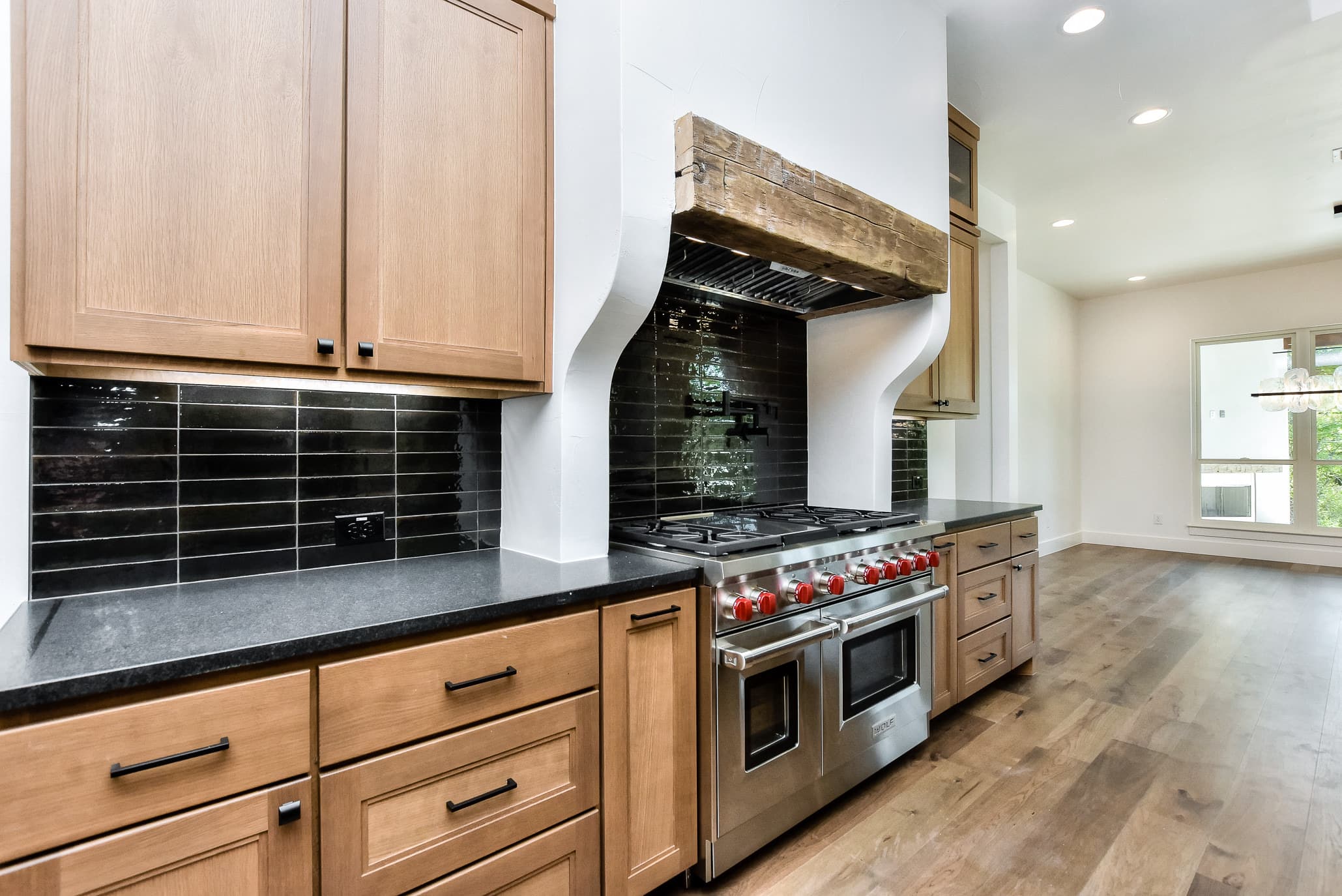 Range with a wood-wrapped plaster hood, black tile backsplash and oak cabinets