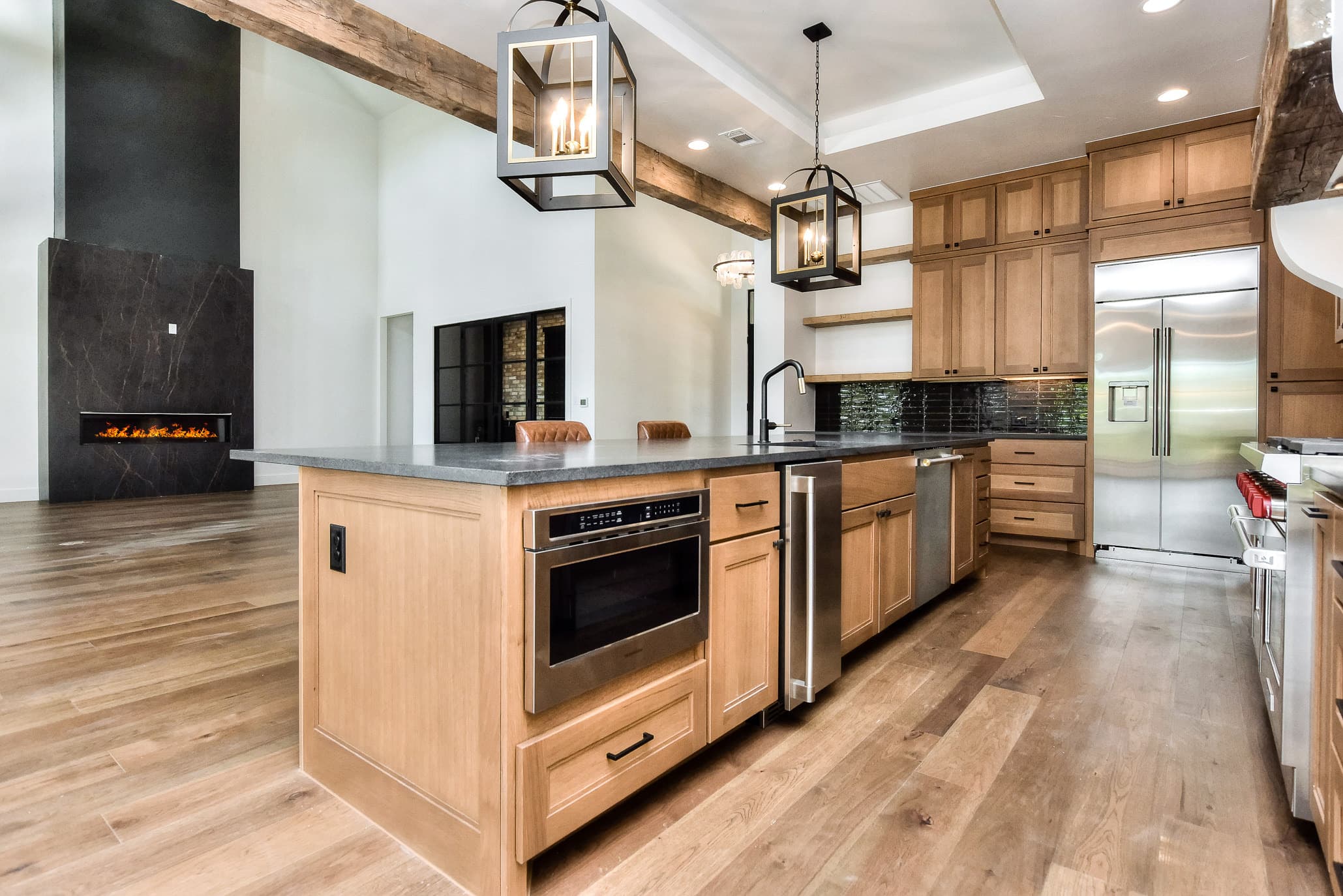 Kitchen island with a microwave drawer, pendant lights and a linear fireplace in the great room beyond