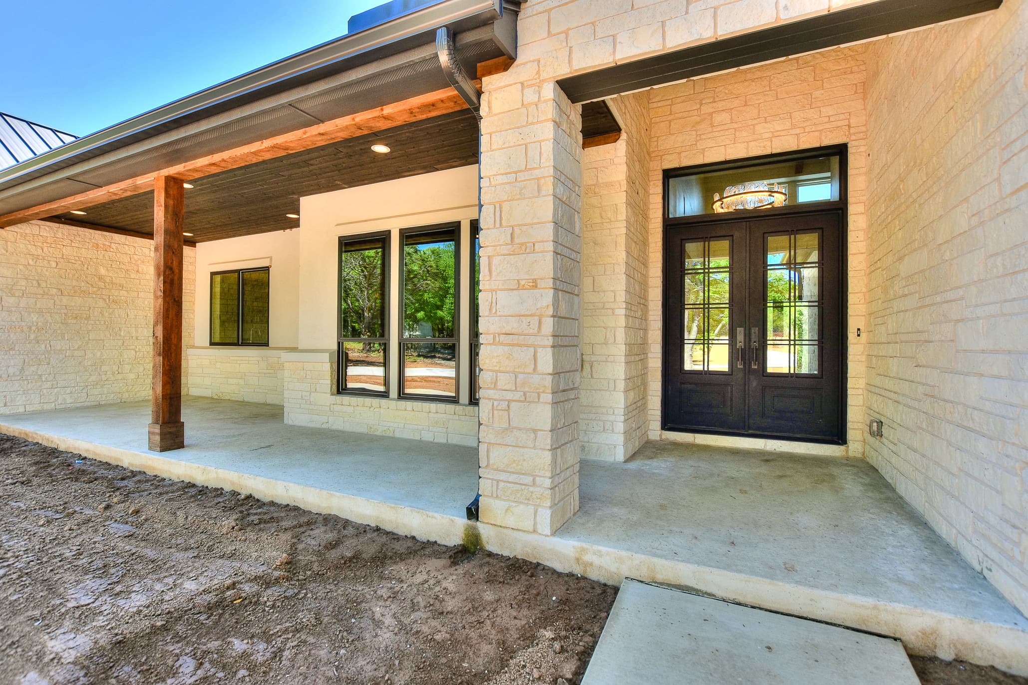 Limestone-clad covered entry with wood posts and a double iron-framed front door