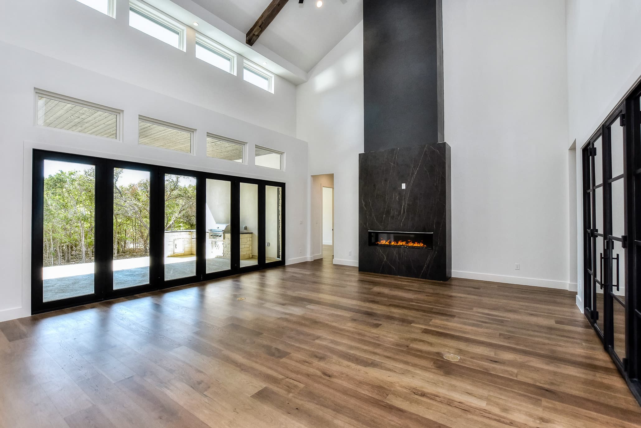 Great room with a tall dark stone fireplace, clerestory windows and folding glass walls to the patio