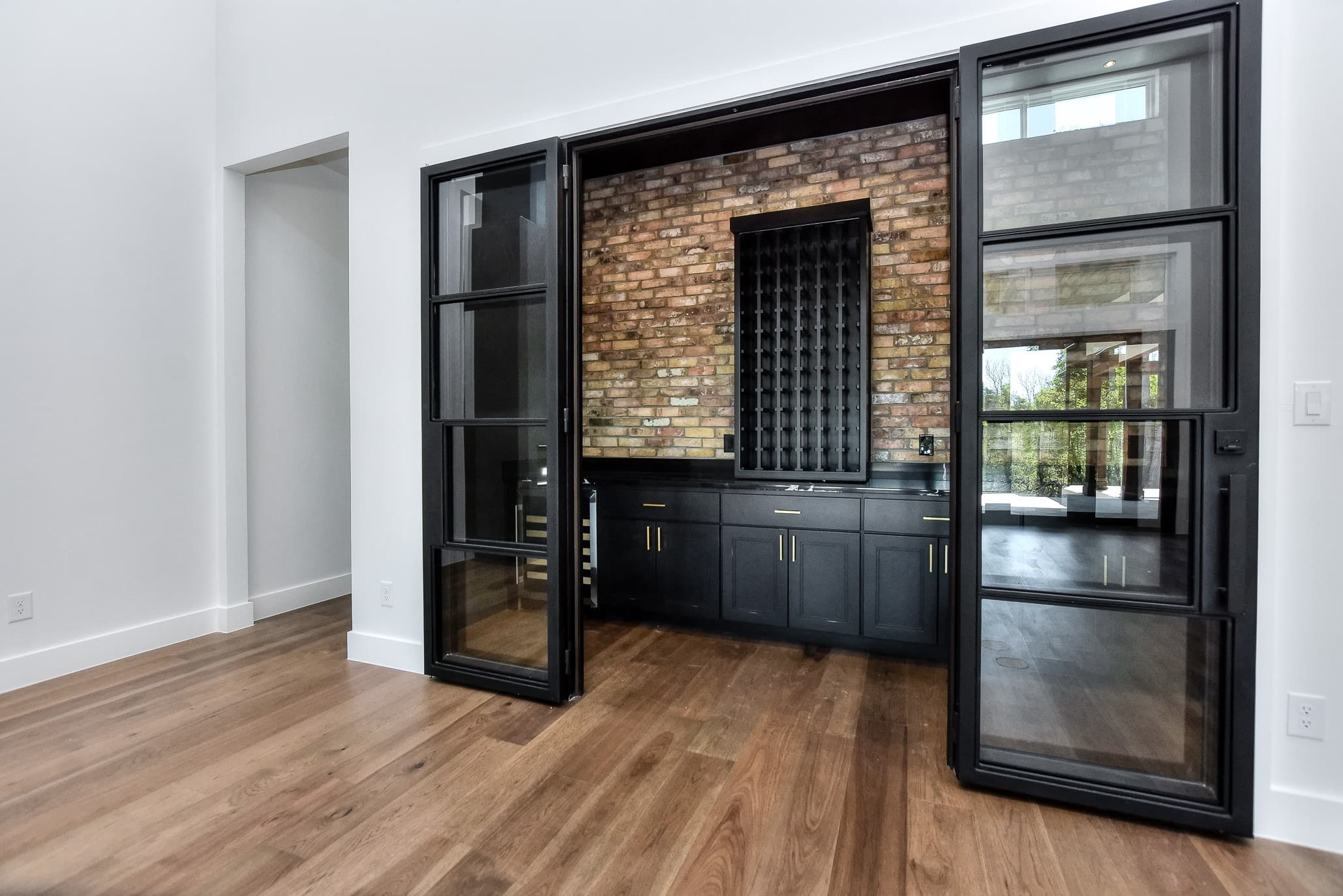Built-in wet bar with navy cabinets and wine storage set against a brick wall behind steel-framed glass doors