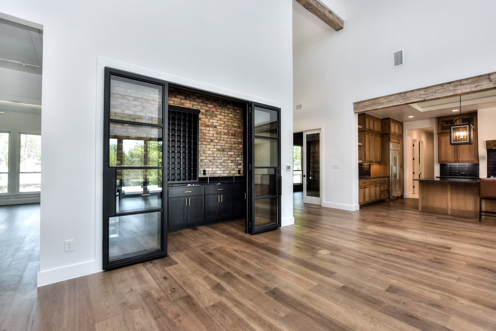 Steel-framed glass-door wine and bar room with brick feature wall, open to the kitchen beyond