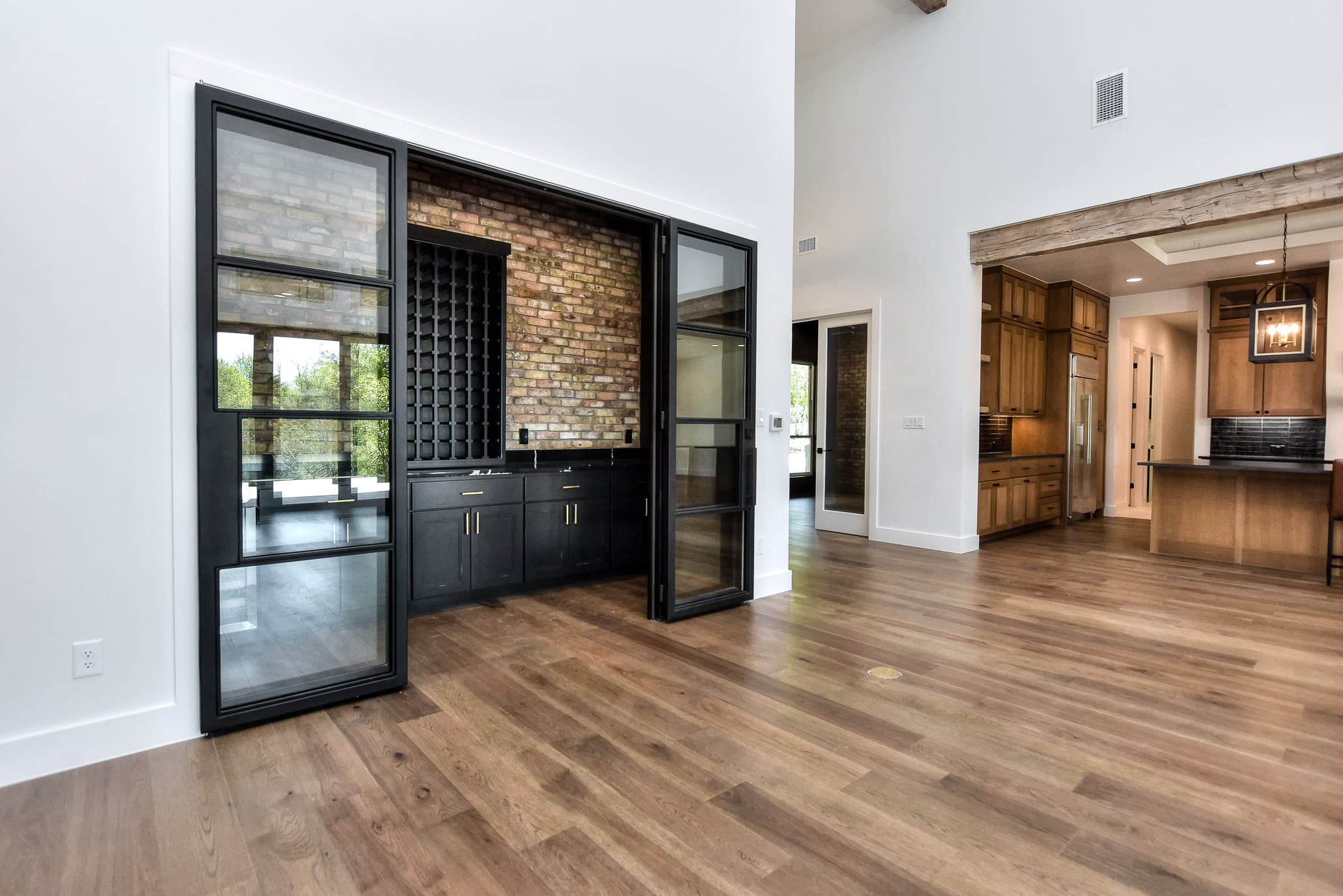 Wine room with brick wall, navy cabinetry and black steel glass doors off the great room
