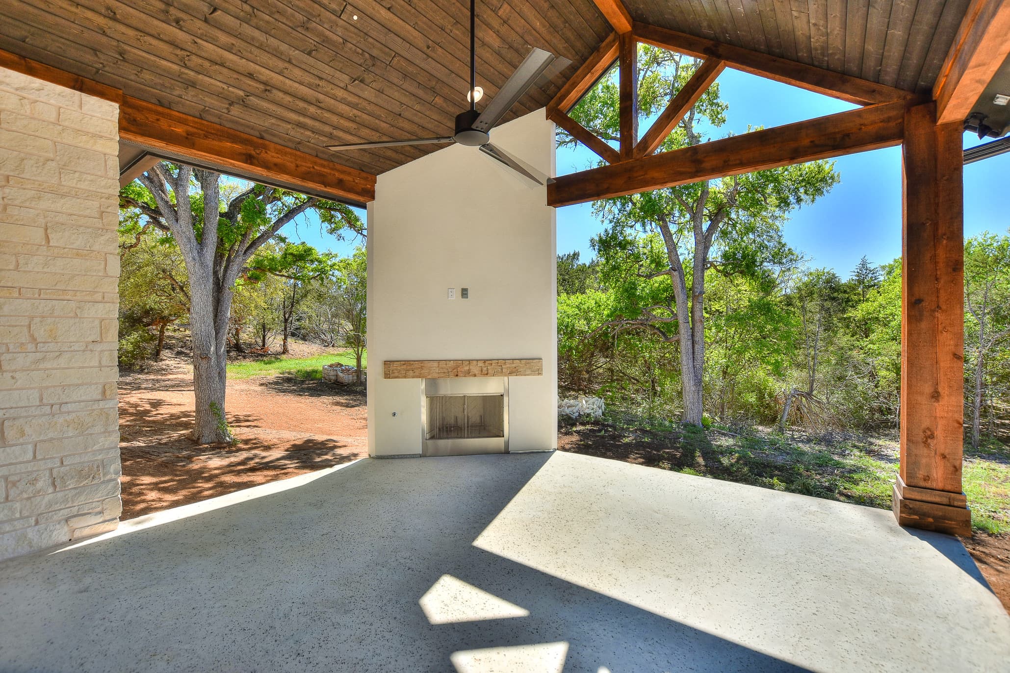 Covered patio with a stained wood ceiling, timber posts, ceiling fan and outdoor fireplace