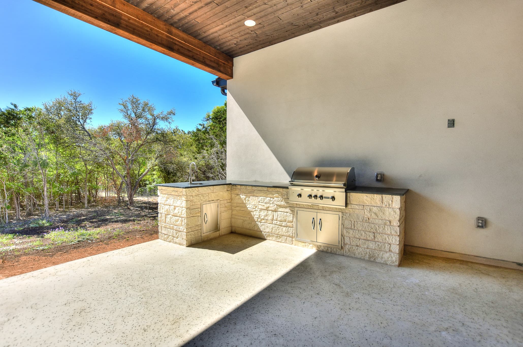 Outdoor kitchen with a built-in grill in a limestone counter under a covered patio