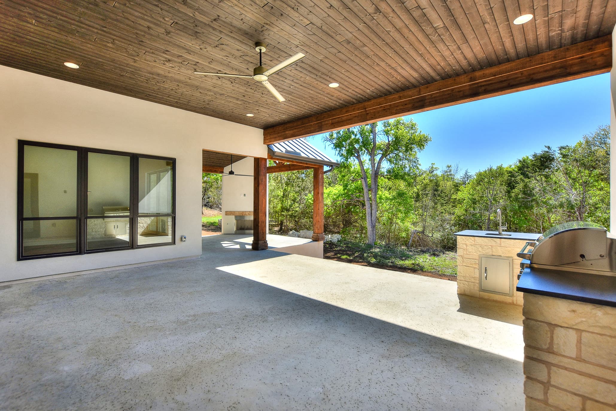 Covered patio with a wood plank ceiling, ceiling fan and limestone outdoor kitchen