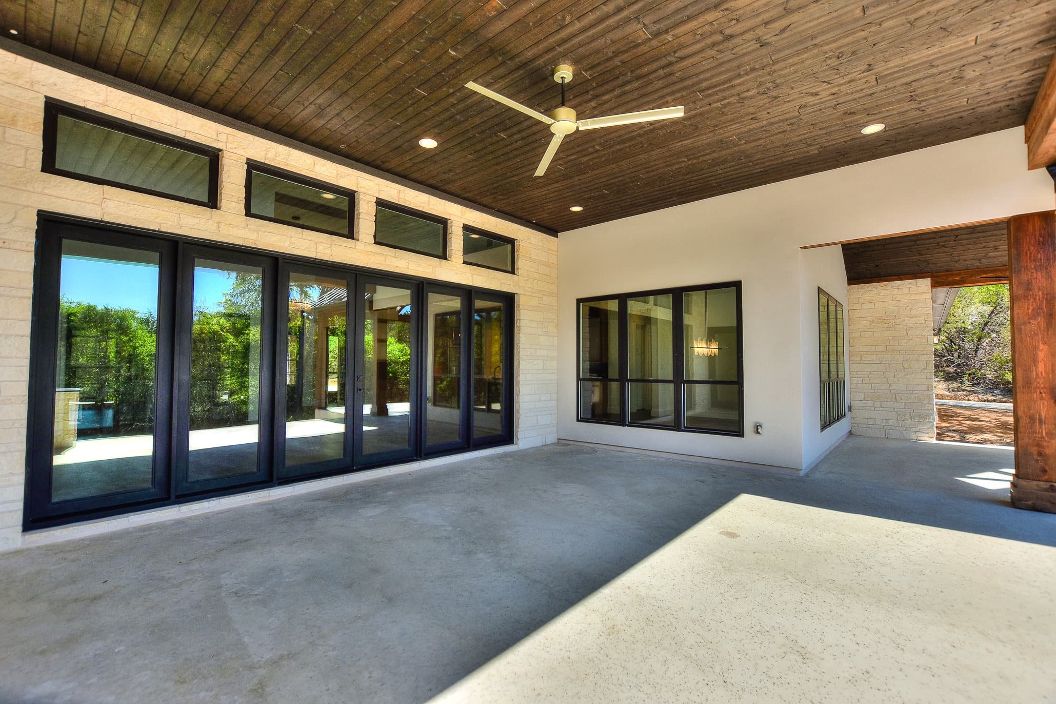 Covered patio with a wood ceiling and a wall of black-framed glass doors and windows