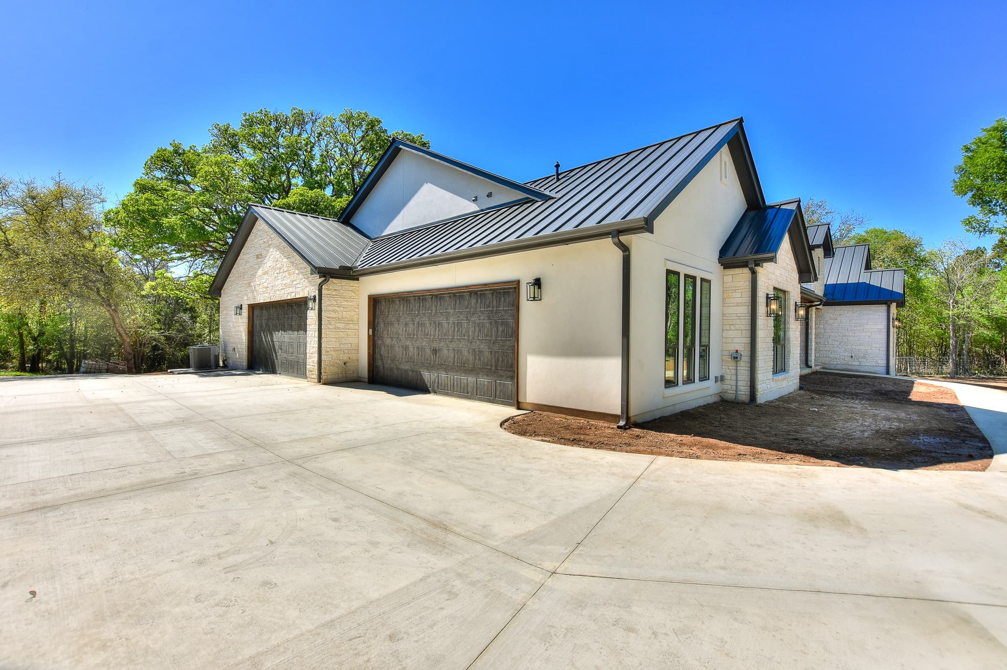 Rear of a white and limestone home with a metal roof and a multi-bay garage