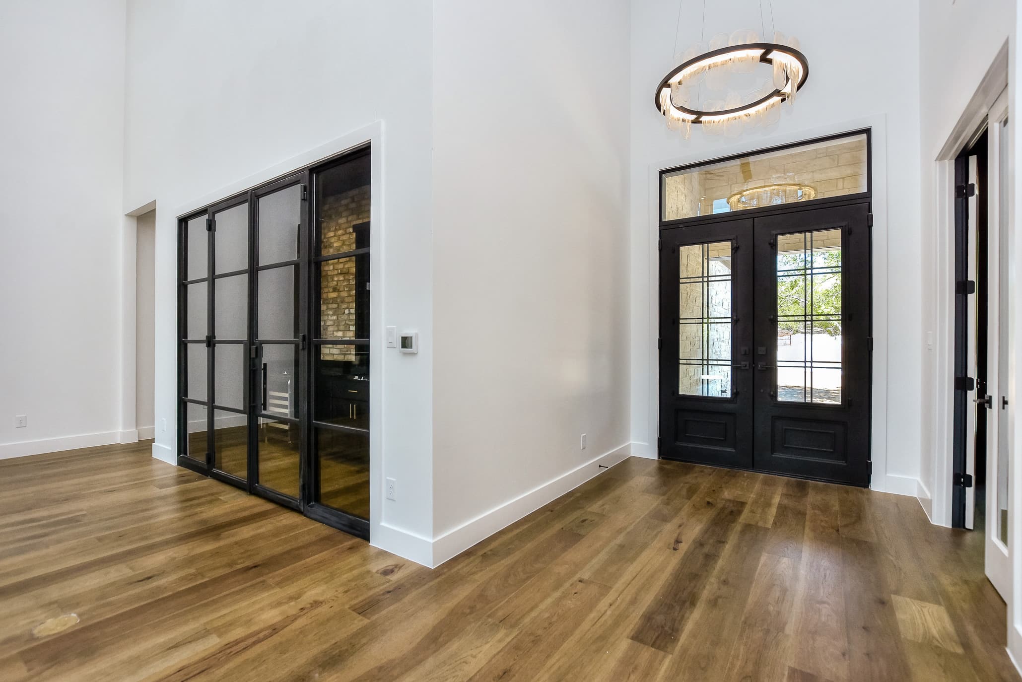 Entry hall with a ring chandelier, black double doors and steel-framed glass wine room