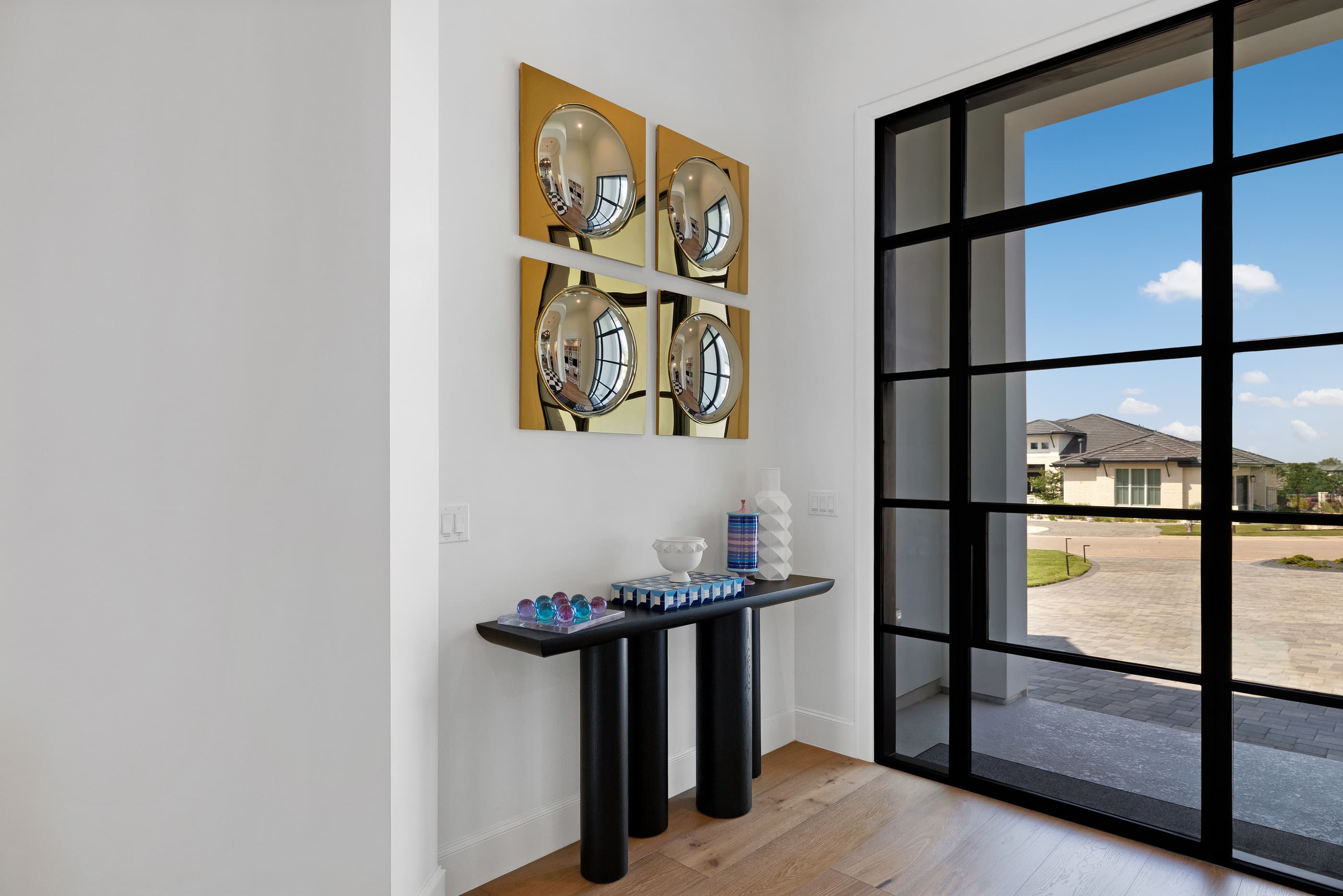 Entry with a black steel-framed glass door, console table and gold convex mirror art on a white wall