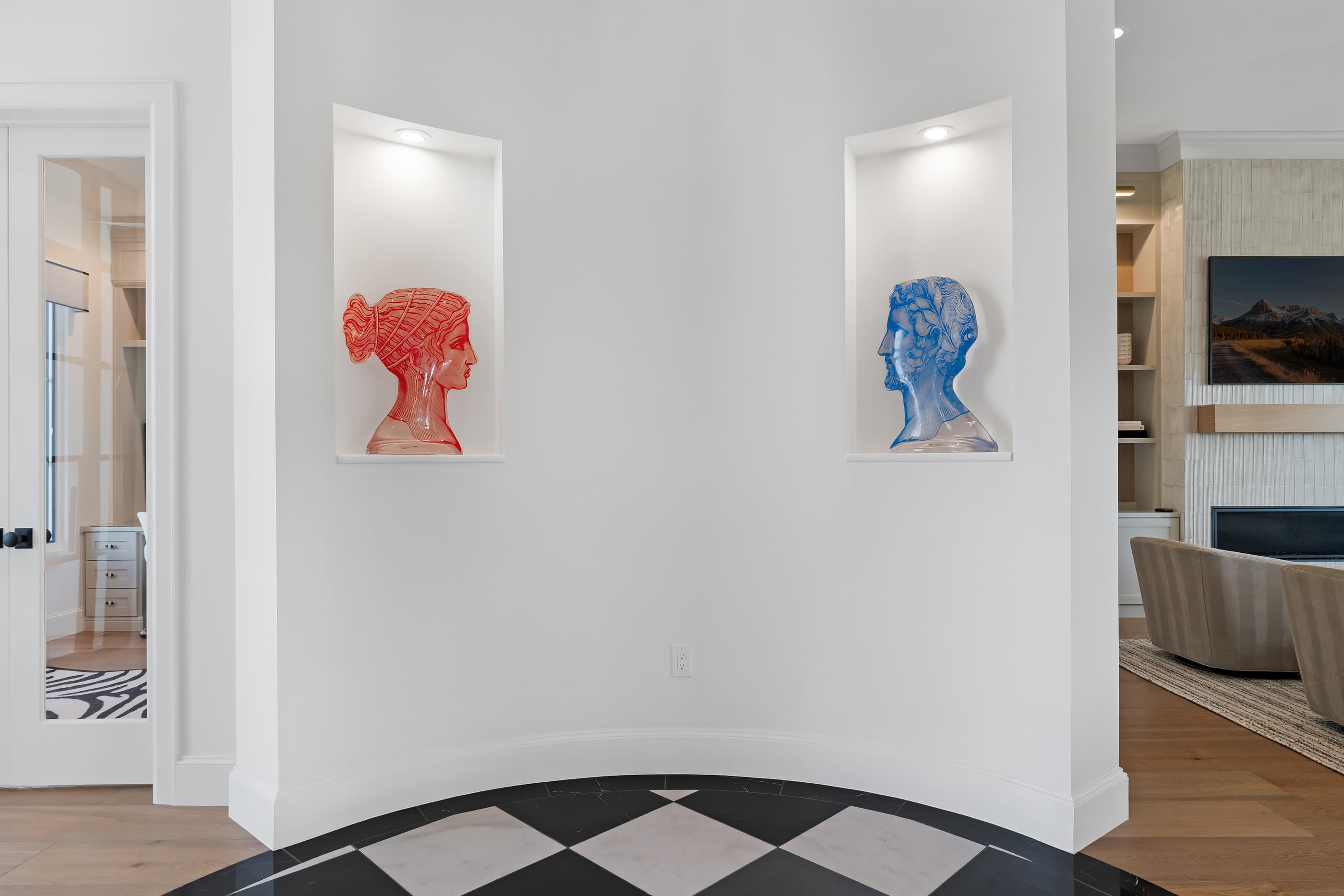 Curved entry wall with lit art niches holding colorful sculptures above a black-and-white checkerboard floor