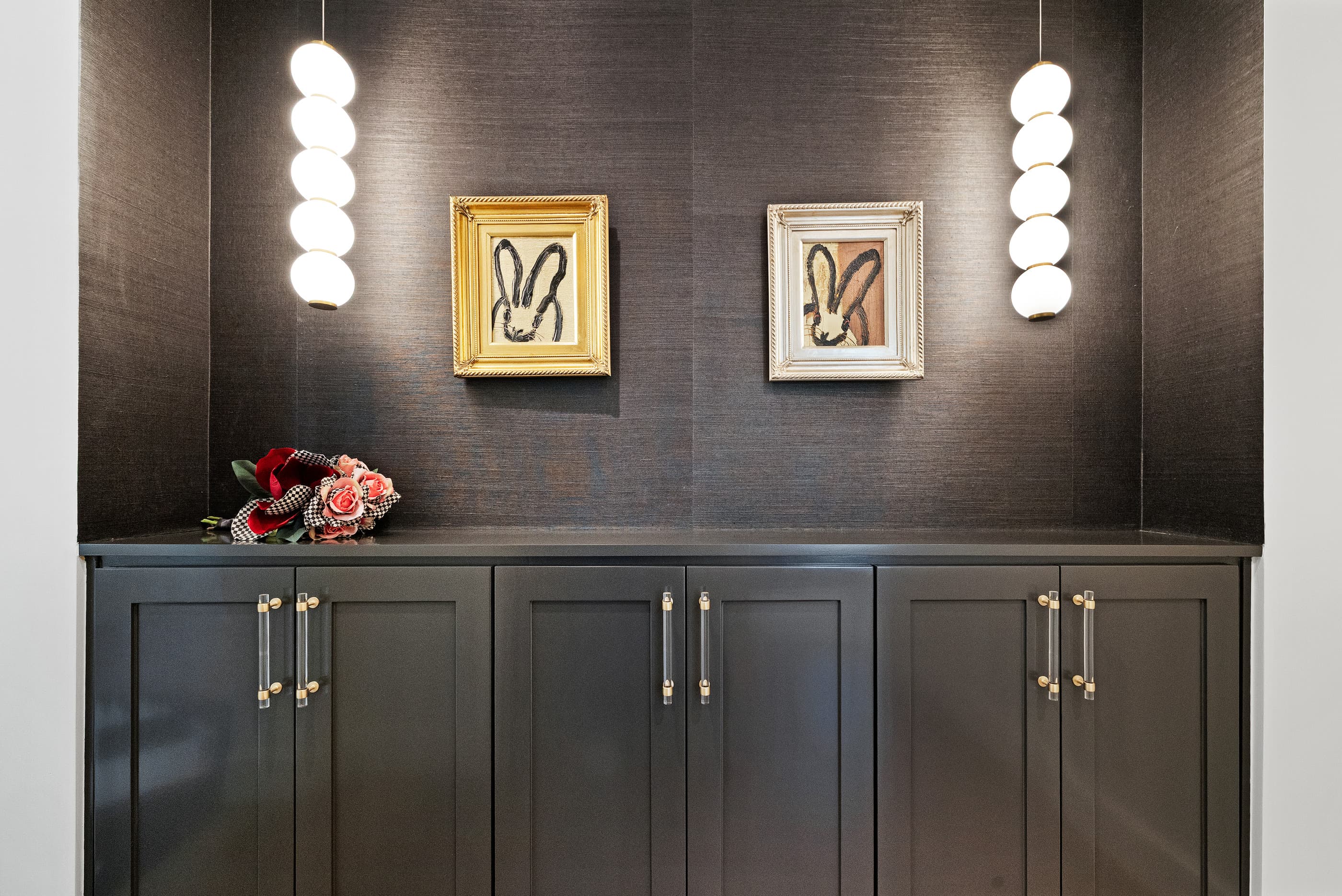 Dark grasscloth wall with a built-in cabinet, brass pulls and glass globe pendant lights