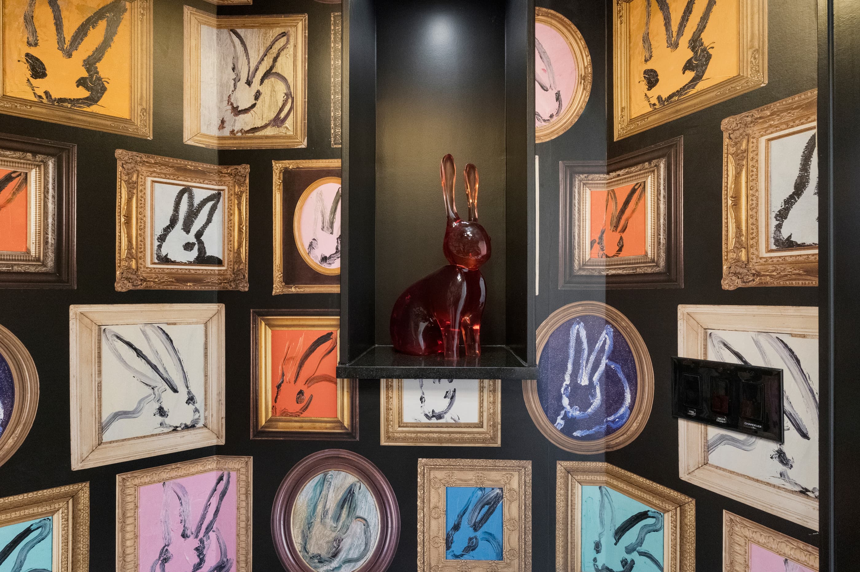 Powder room niche with a red glass rabbit sculpture among colorful framed rabbit paintings