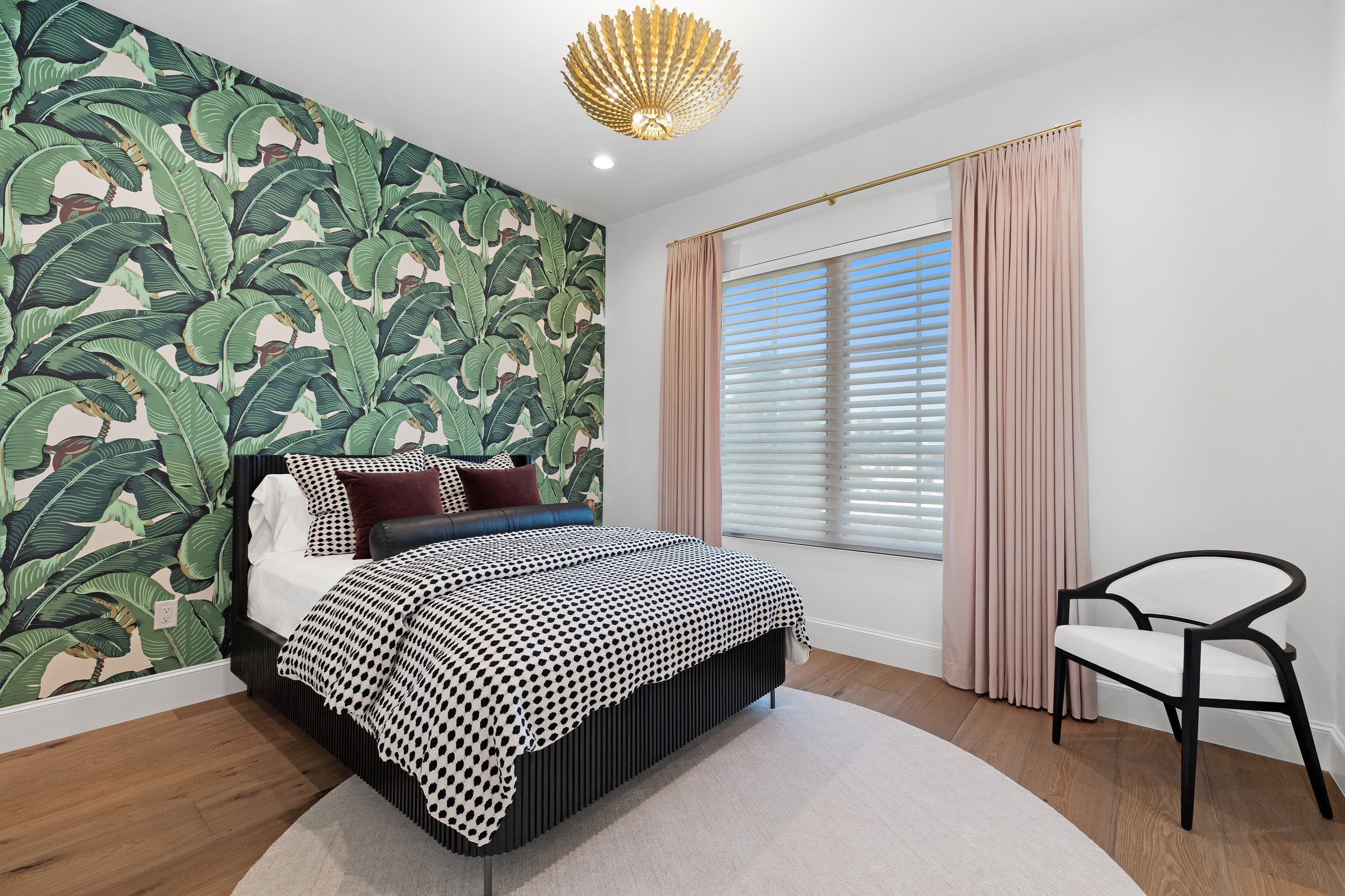 Guest bedroom with banana-leaf wallpaper accent wall, patterned bedding and a shell-shaped ceiling light
