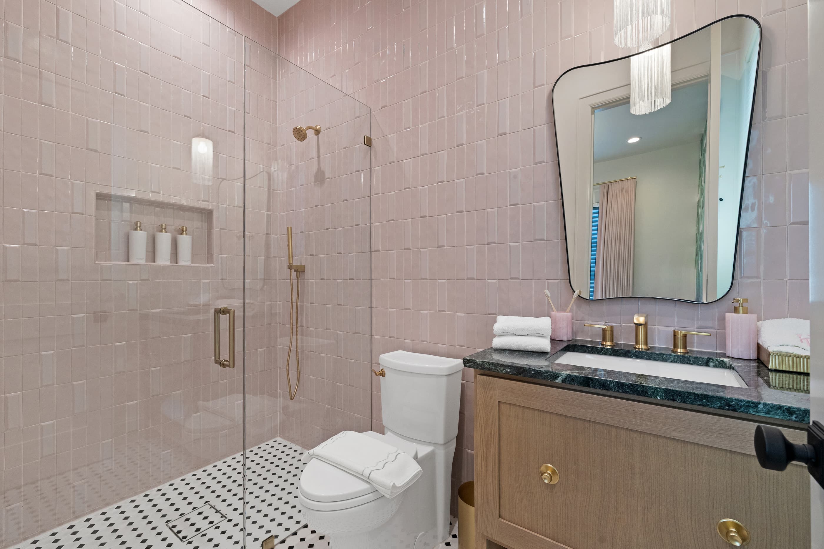 Bathroom with pink handmade-style wall tile, glass shower, brass fixtures and a green stone vanity top