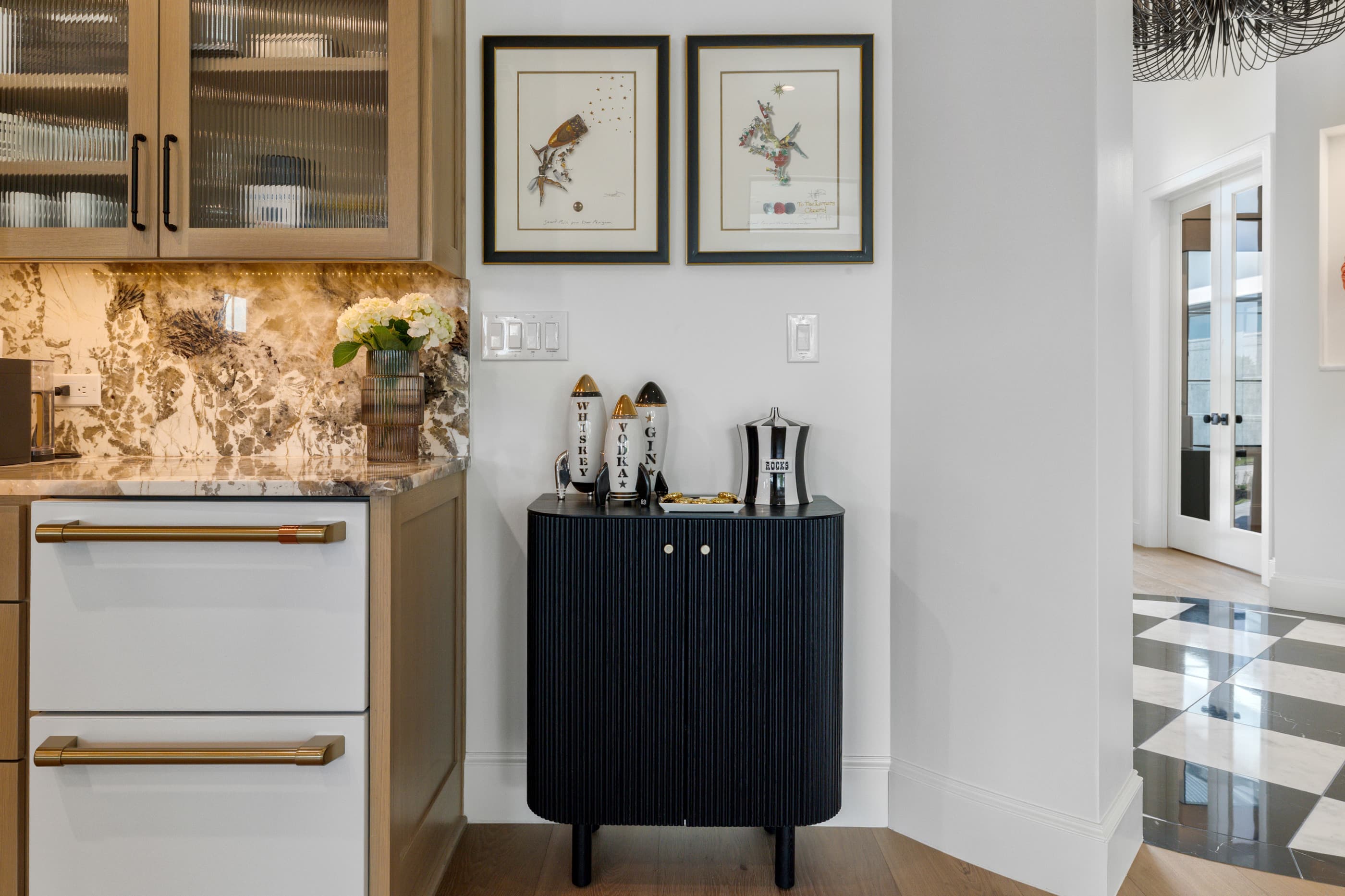 Kitchen corner with a black fluted cabinet, framed botanical prints and a view to checkerboard flooring