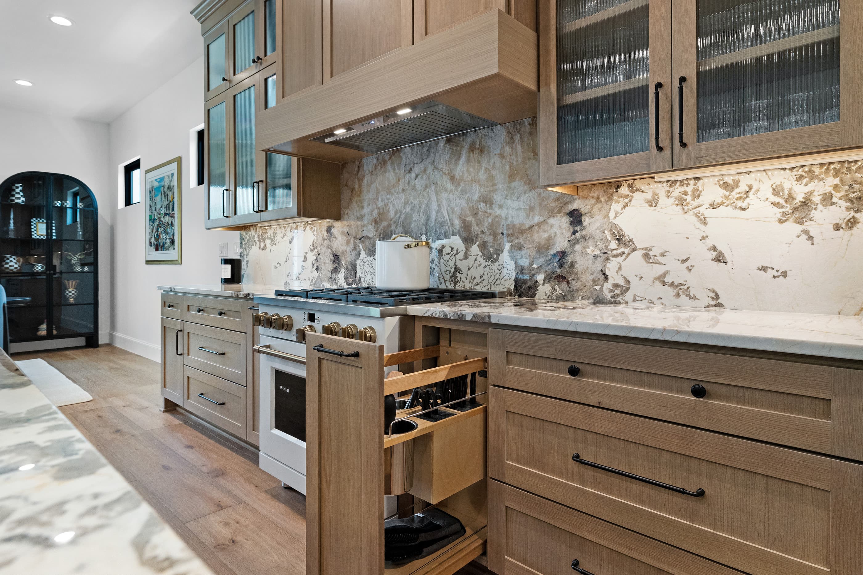 Chef's kitchen with white range, natural stone backsplash and pull-out utensil organizer in oak cabinets