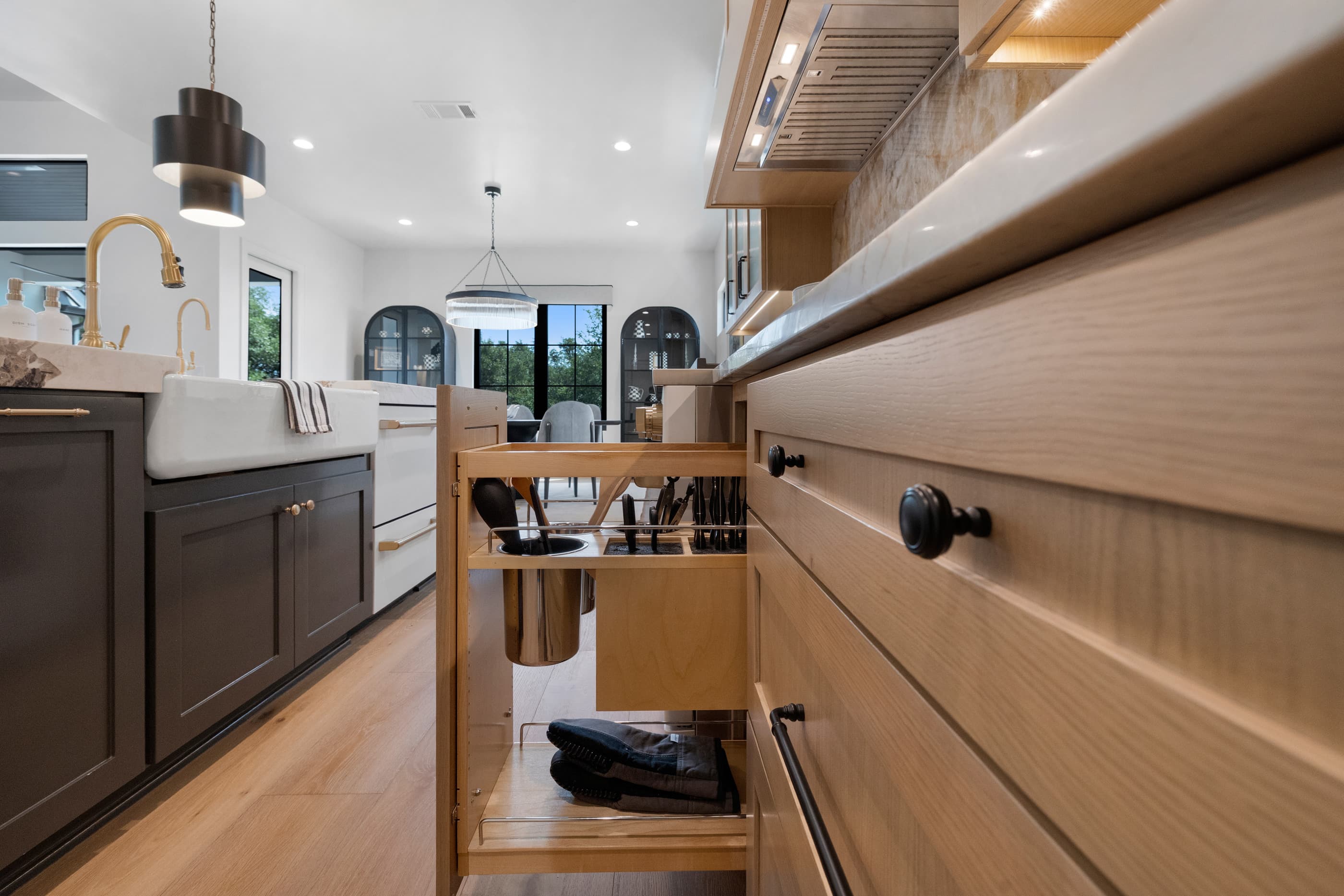 Kitchen cabinetry detail with pull-out tray storage and a farmhouse sink beneath a pendant light
