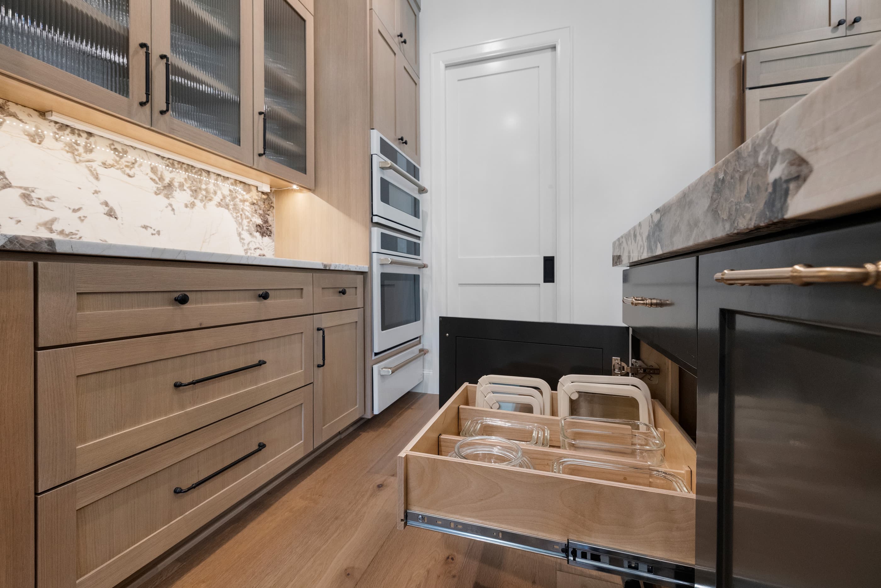 Kitchen drawer pulled open showing food storage containers beside built-in wall ovens