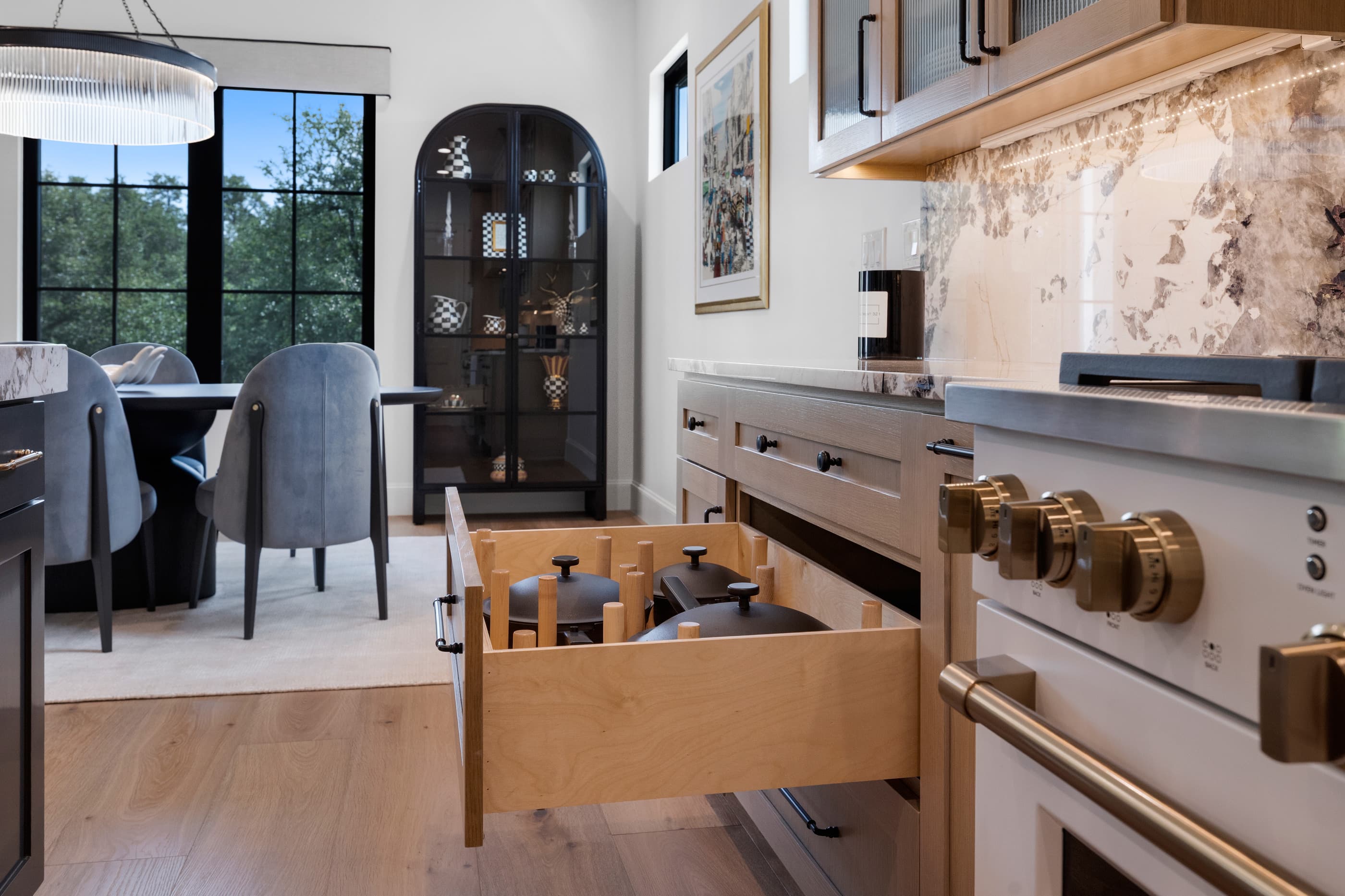Deep kitchen drawer with cookware beneath a gas range with brass knobs, dining area beyond