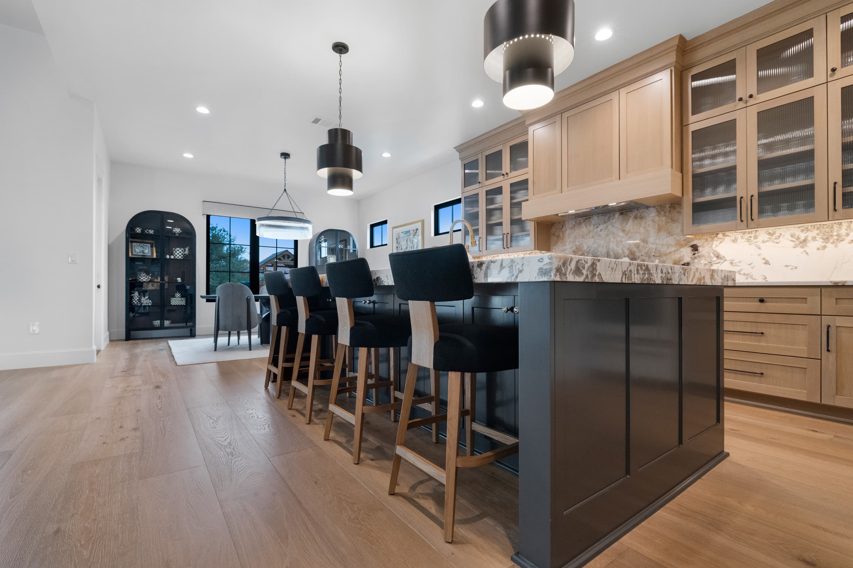 Kitchen island with black cabinetry and bar stools, glass-front oak cabinets and arched display cabinet in the dining area