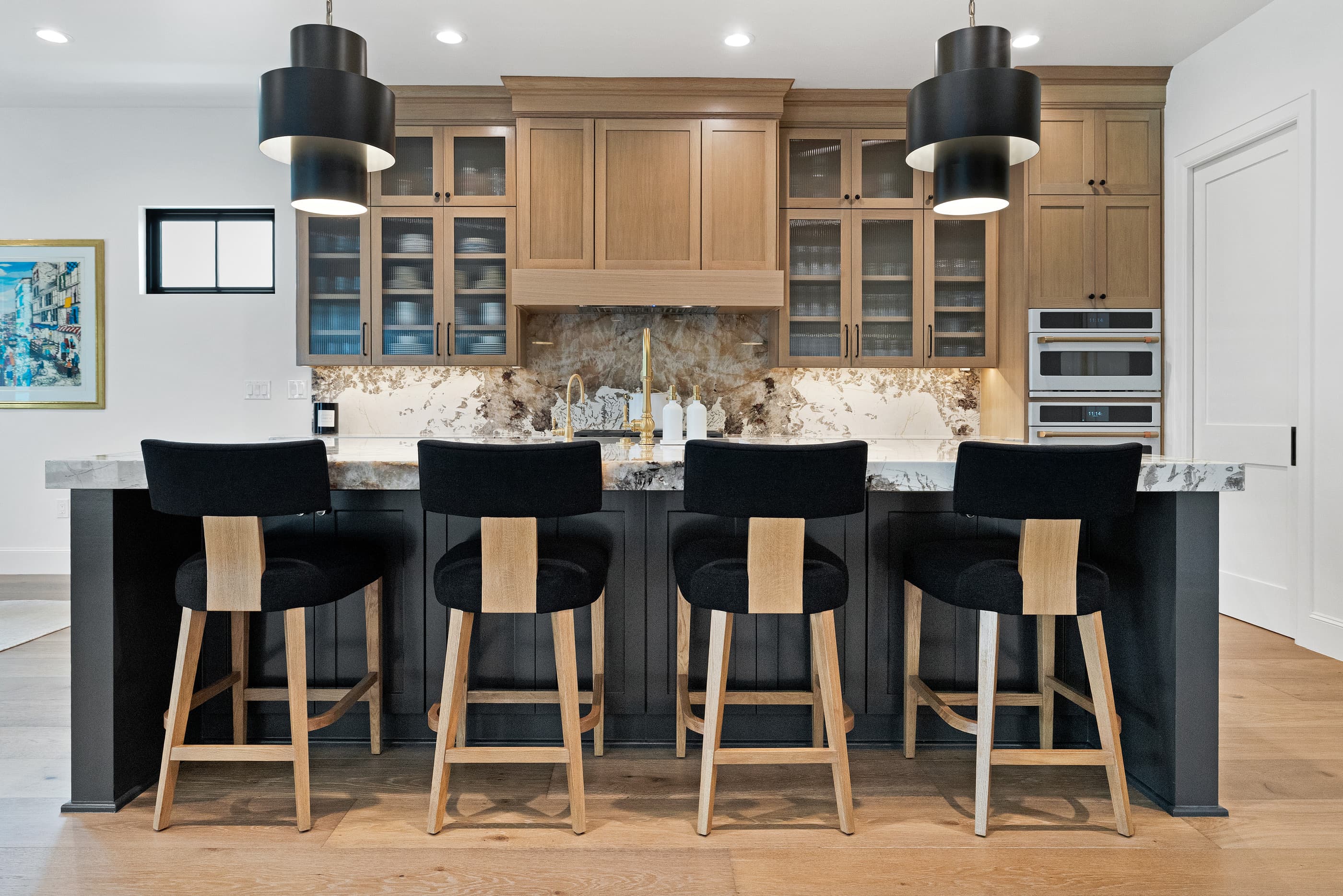Kitchen island with four black upholstered counter stools beneath black pendant lights