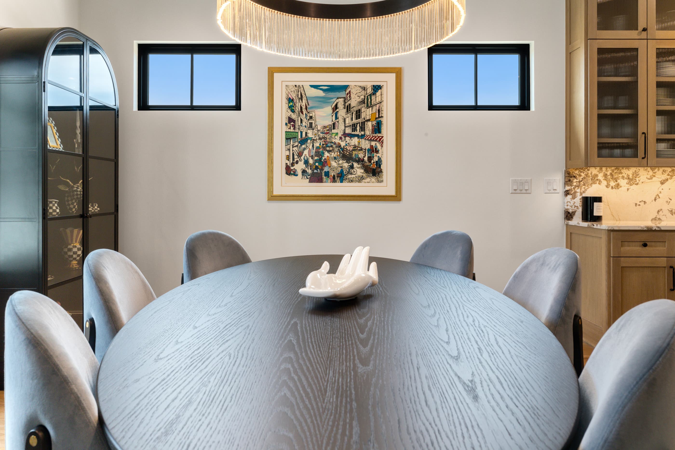 Formal dining room with an oval black table, velvet chairs and a beaded chandelier