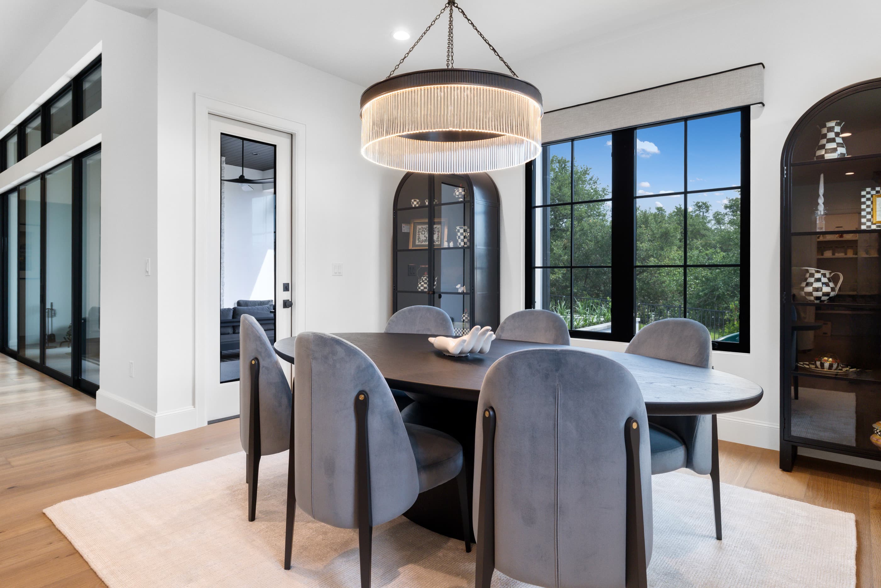 Dining room with an oval table, gray upholstered chairs, fringe chandelier and black-framed windows