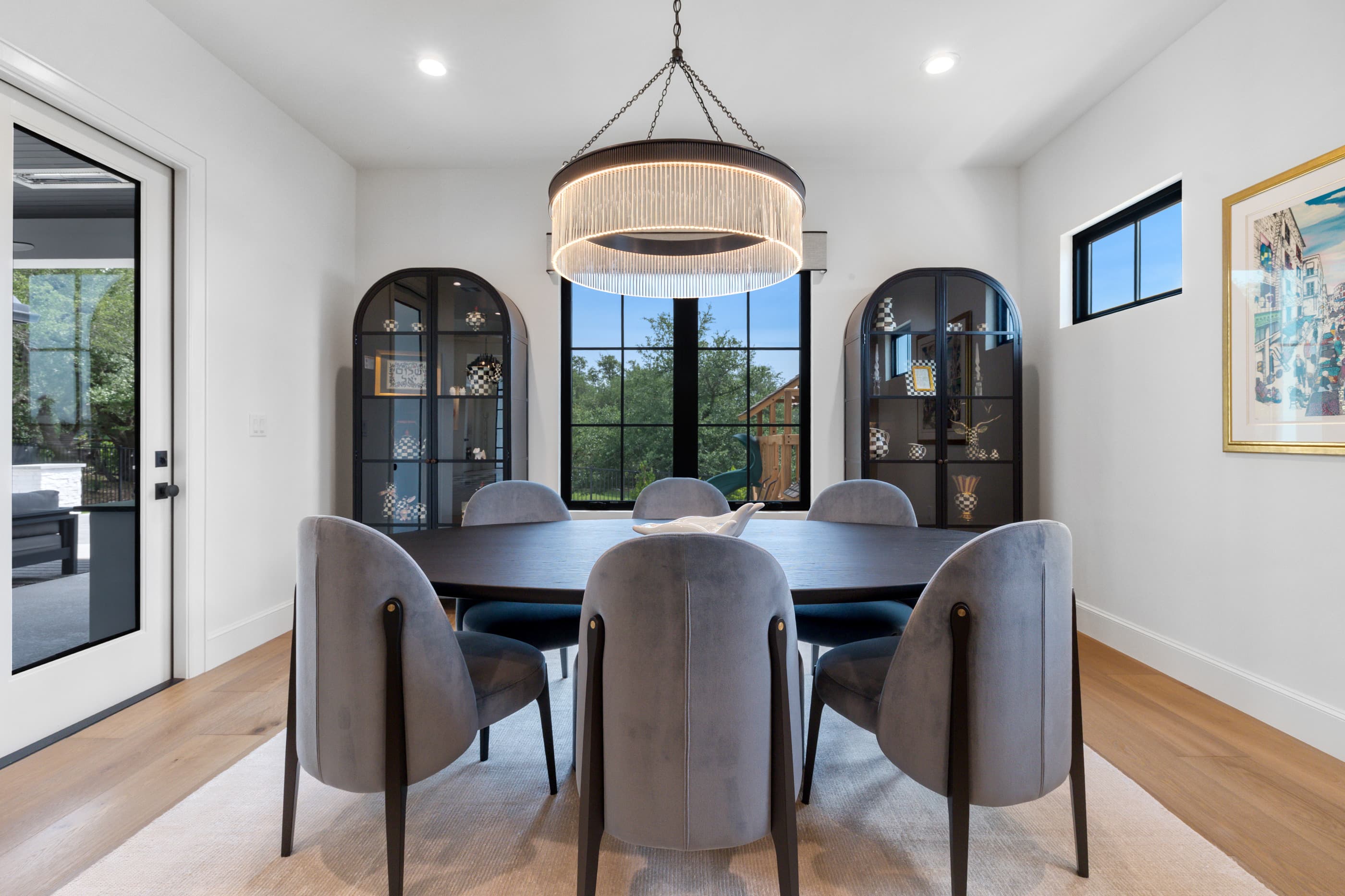 Dining room with a fringe chandelier, two arched black display cabinets and steel-framed windows