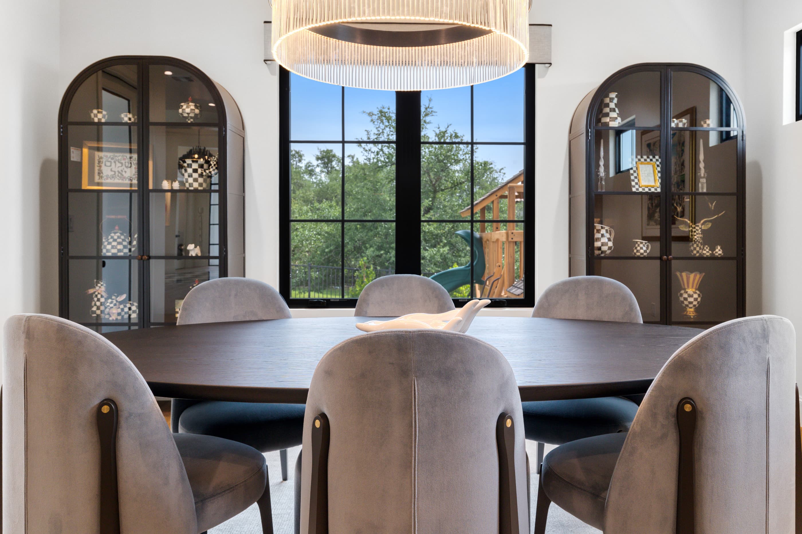 Arched black display cabinets flanking a window in a formal dining room with velvet chairs