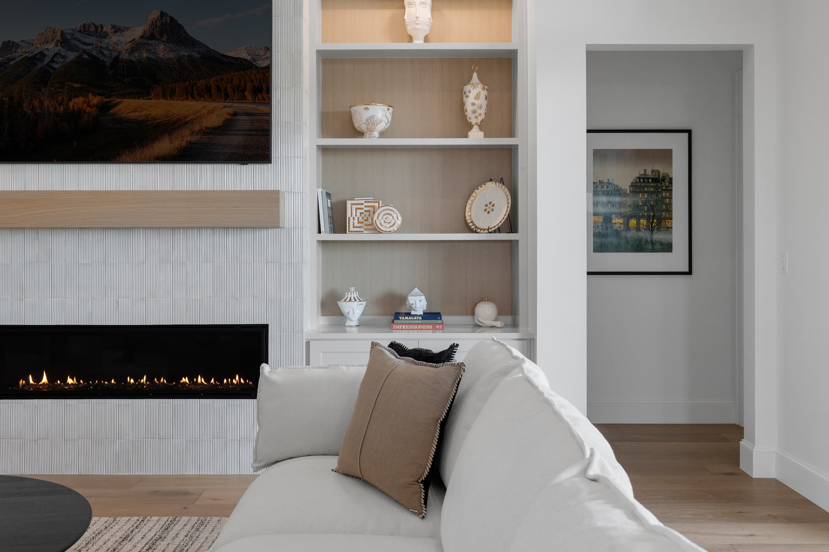 Living room seating area with a linear fireplace, white built-ins with oak backing and a white sofa